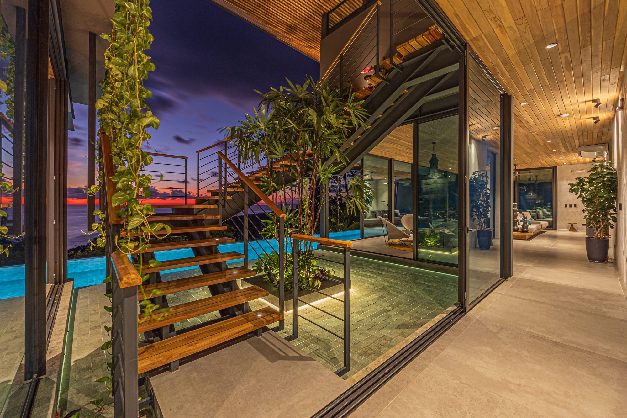 Wood and metal staircase with sunset ocean view over an infinity pool.