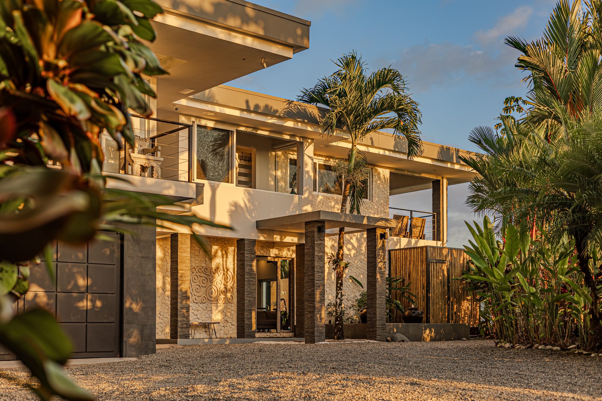 Fachada de casa moderna de dos pisos rodeada de palmeras al atardecer.