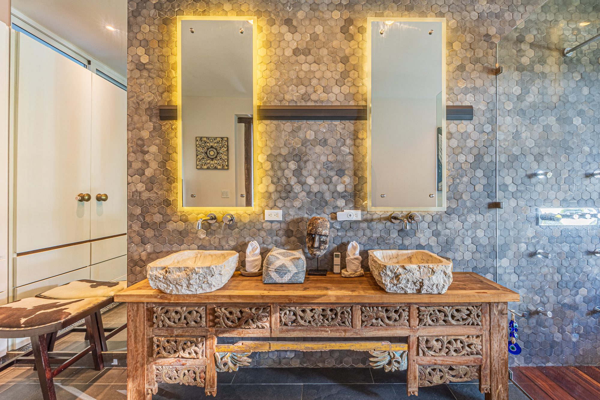 Bathroom with dual stone sinks, hexagonal tile wall and backlit mirrors