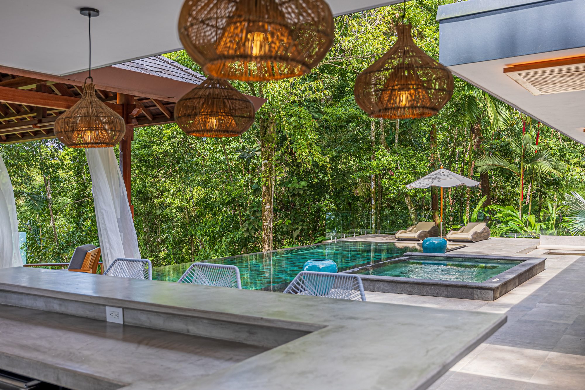 Infinity pool with jacuzzi surrounded by tropical jungle, view from covered terrace