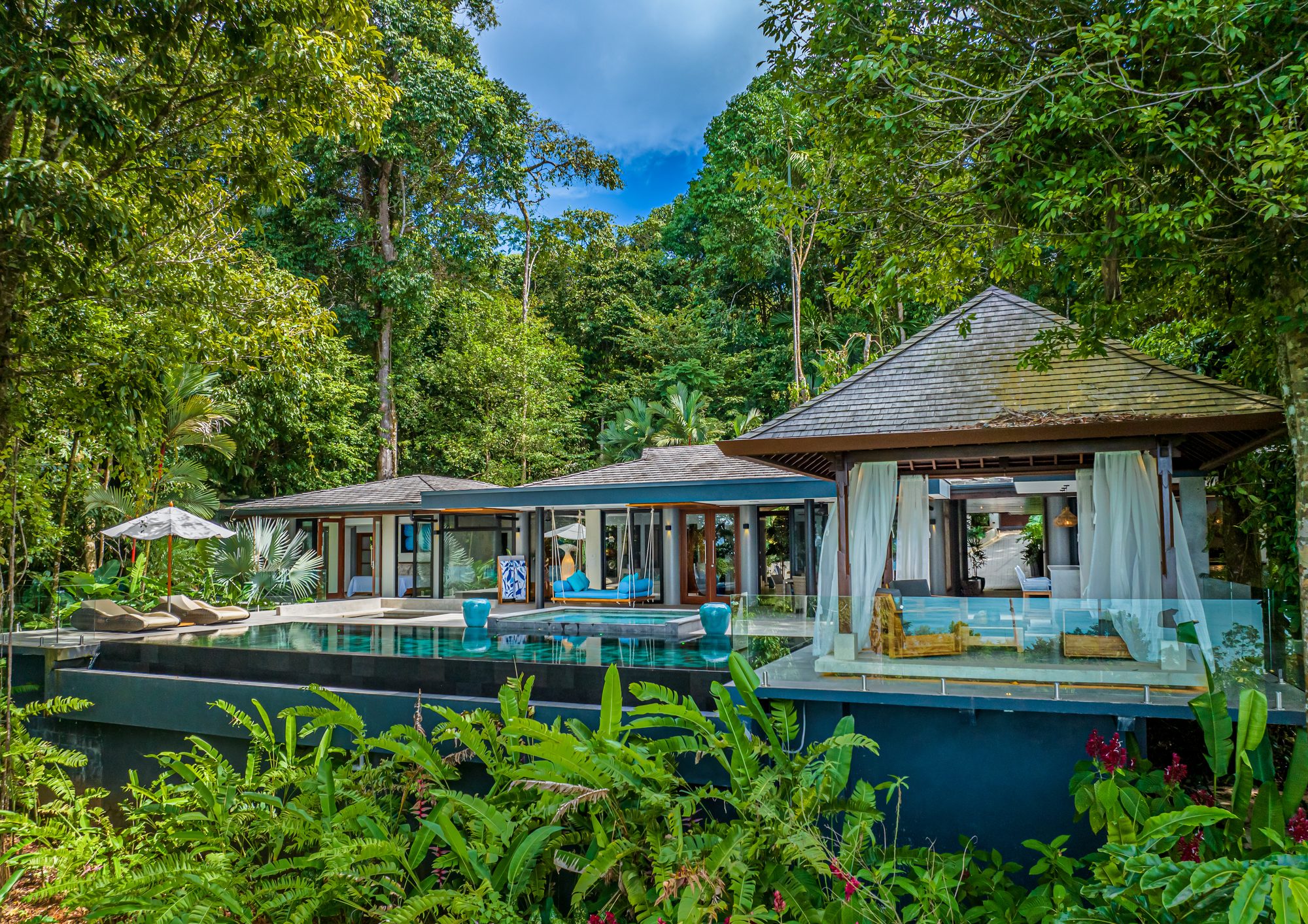 Modern villa with infinity pool surrounded by lush tropical jungle.