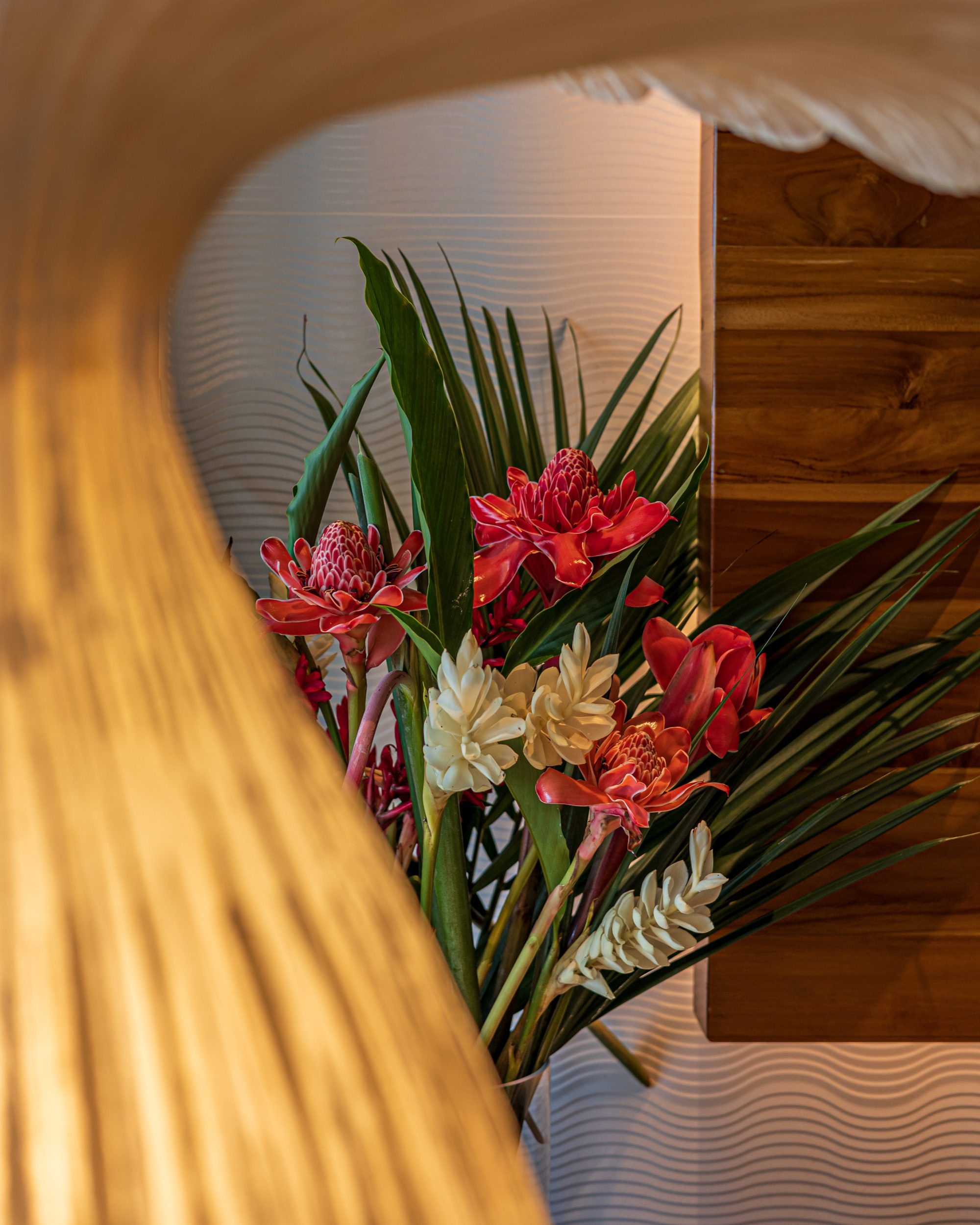 Tropical red and white flower arrangement beside a wooden furniture piece.