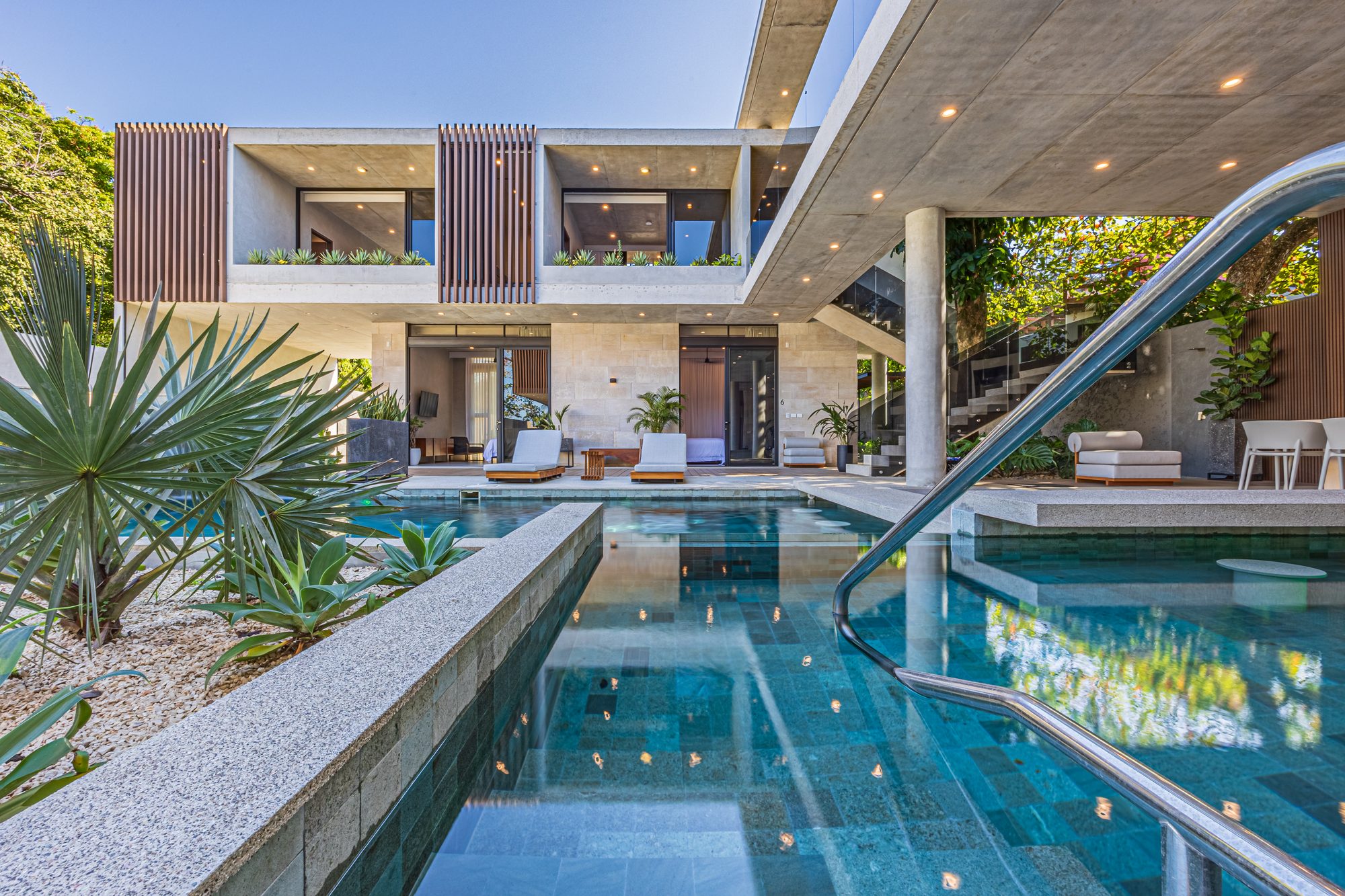 Designer pool with handrail in front of a modern home surrounded by tropical greenery.