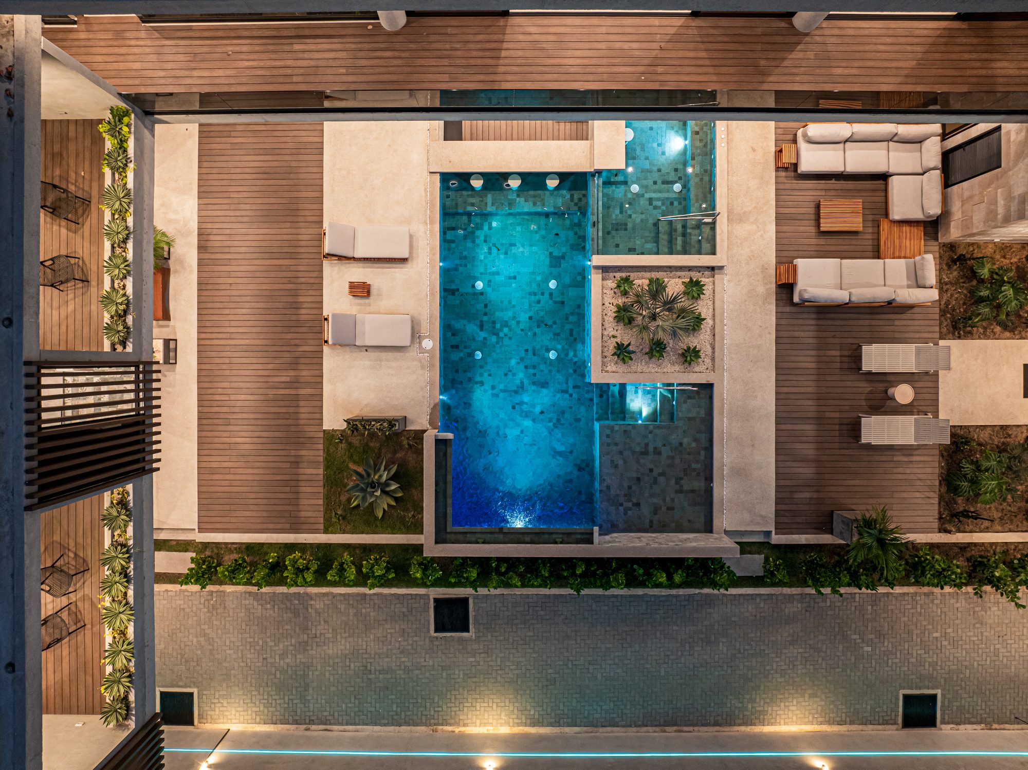 Aerial night view of illuminated pool and lounge area with wood deck
