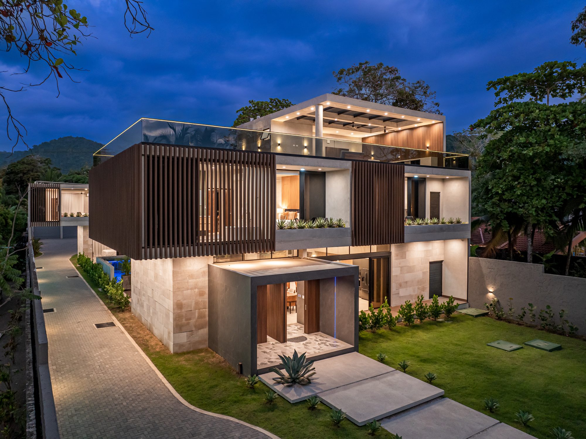 Nighttime view of a modern two-story home with garden and wooden slat screens.