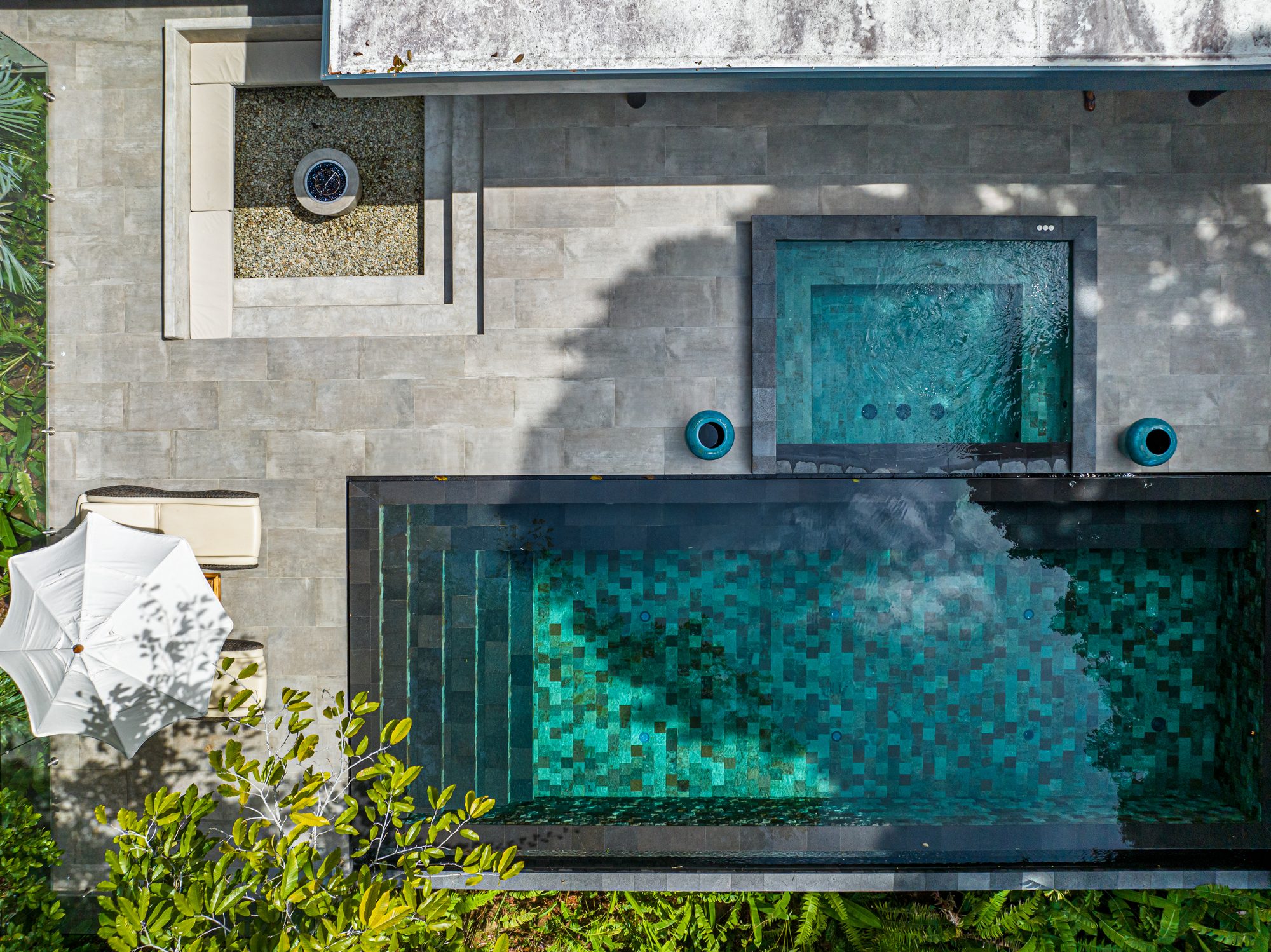 Aerial view of turquoise mosaic pool next to jacuzzi and tropical garden.