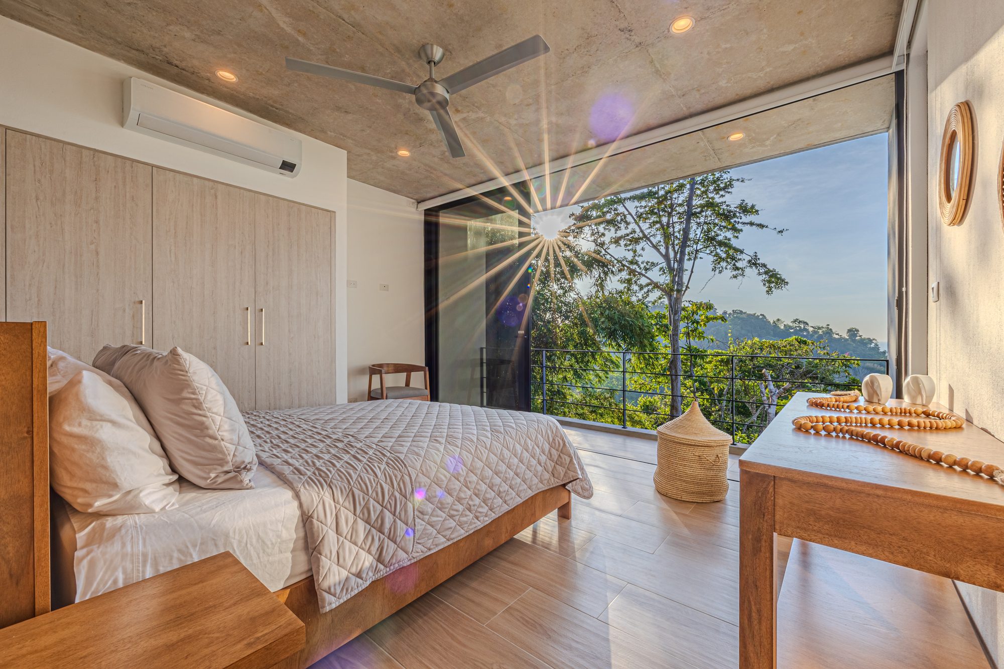 Dormitorio con cama y balcón abierto a la vista de la selva al atardecer.