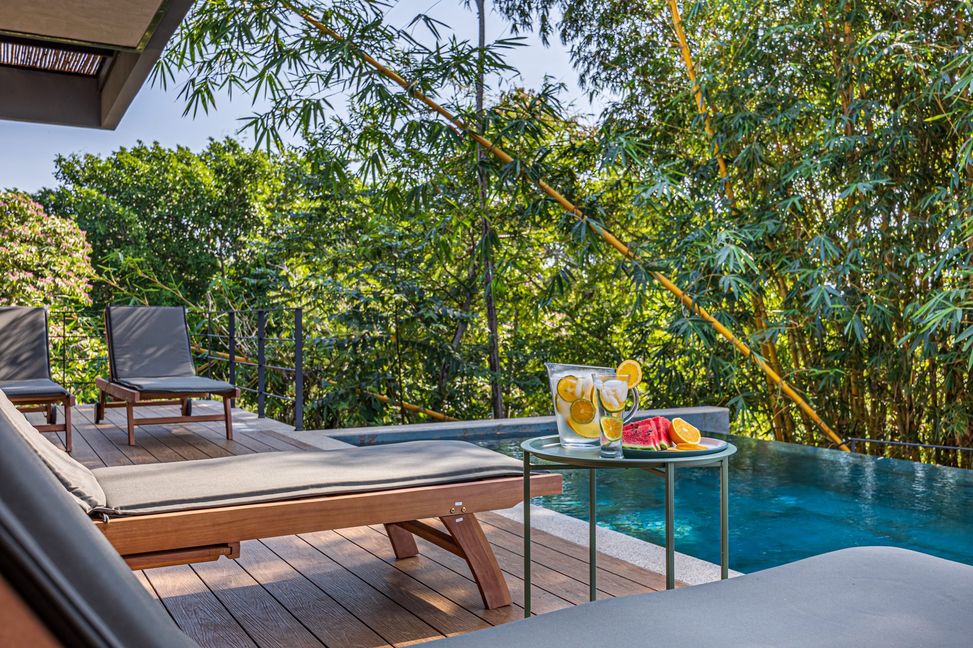 Piscina infinita con bandeja de frutas y bebidas junto a camastros rodeados de bambú