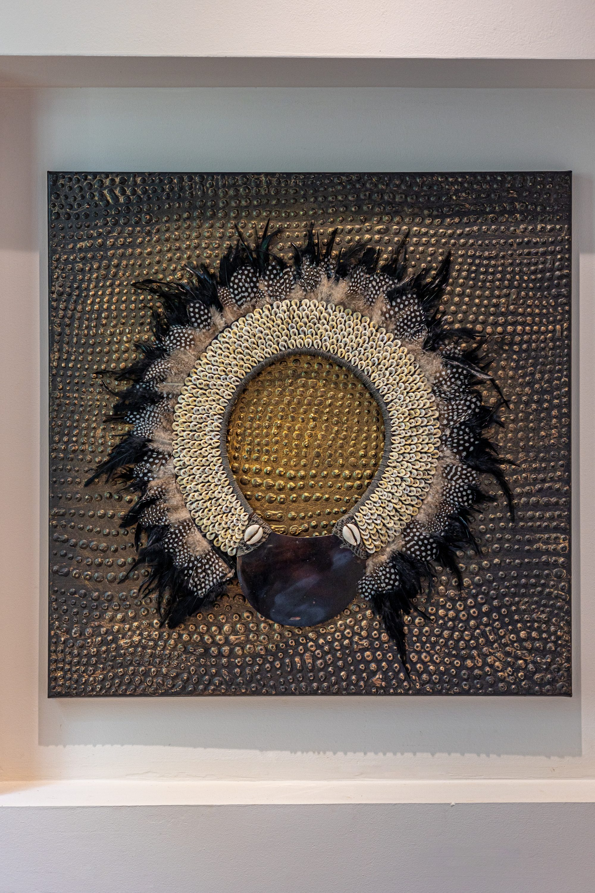 Decorative wall art with shells and feathers mounted on a textured gold wall.