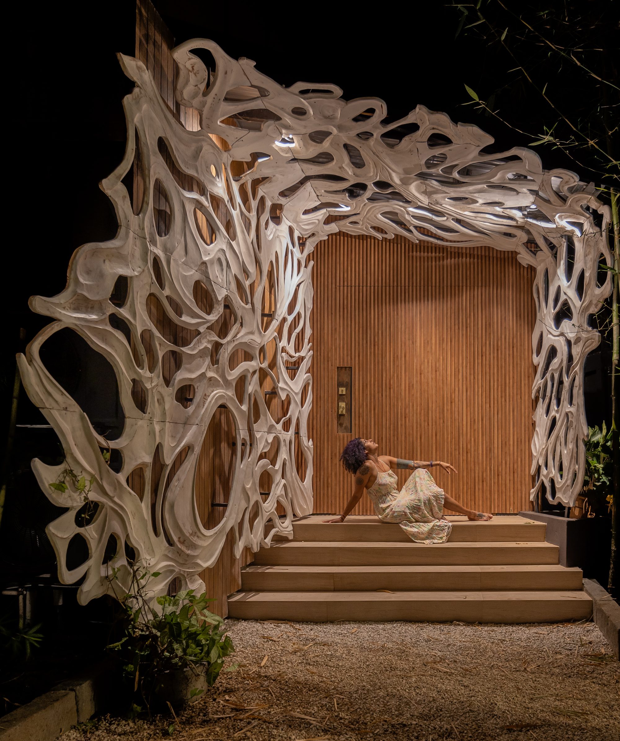 Woman sitting on steps beneath an organic wooden sculpture at a house entrance