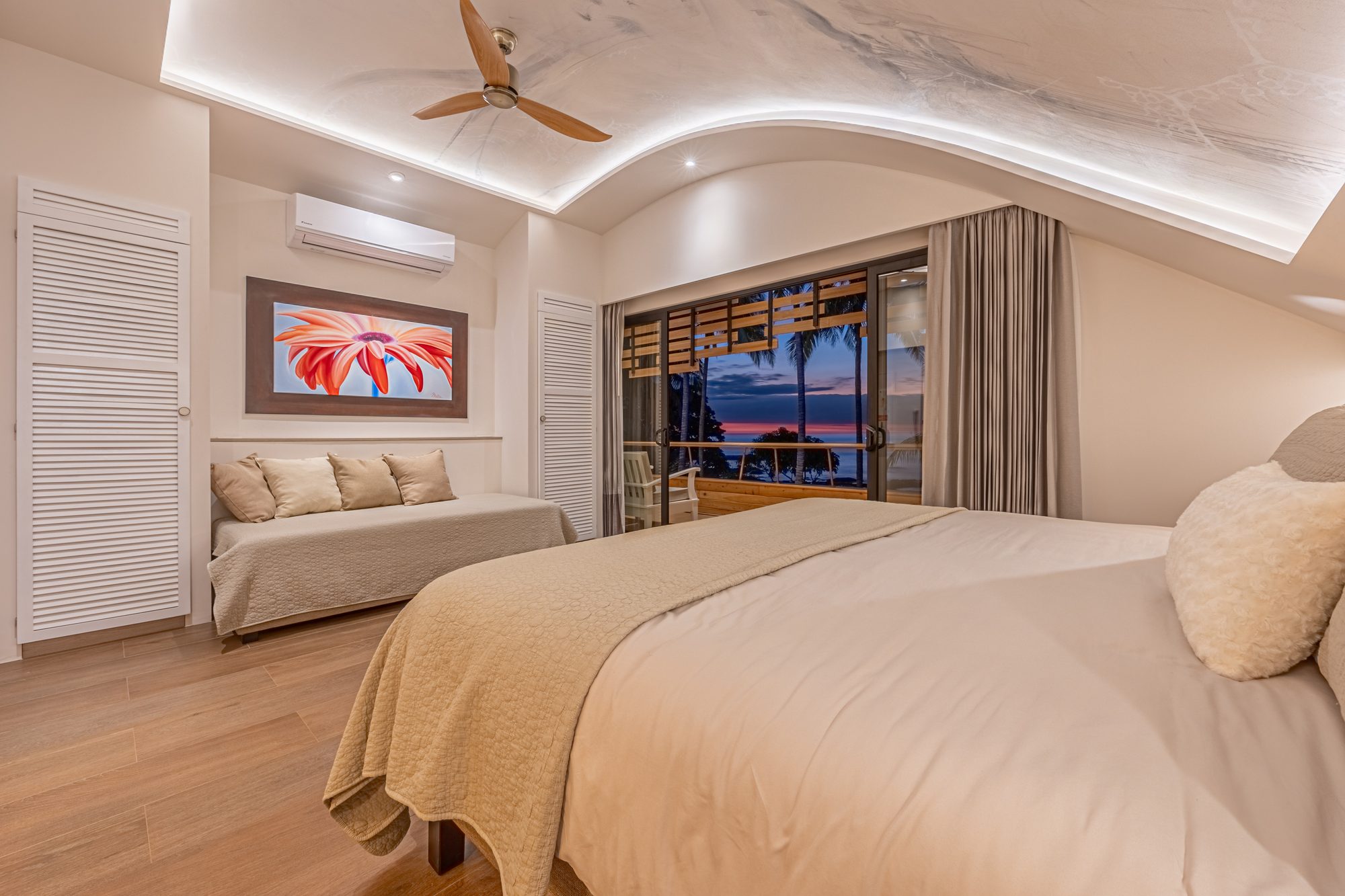 Bedroom with king bed, curved ceiling and sunset view through palm trees.