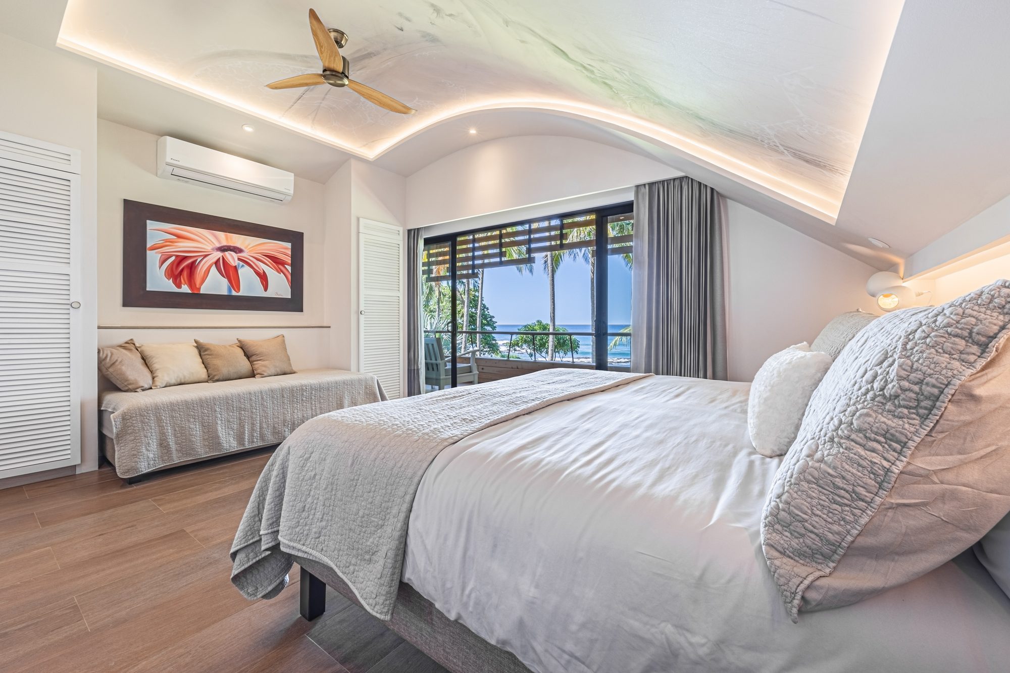 Elegant bedroom with ocean view and palm-lined balcony at sunset
