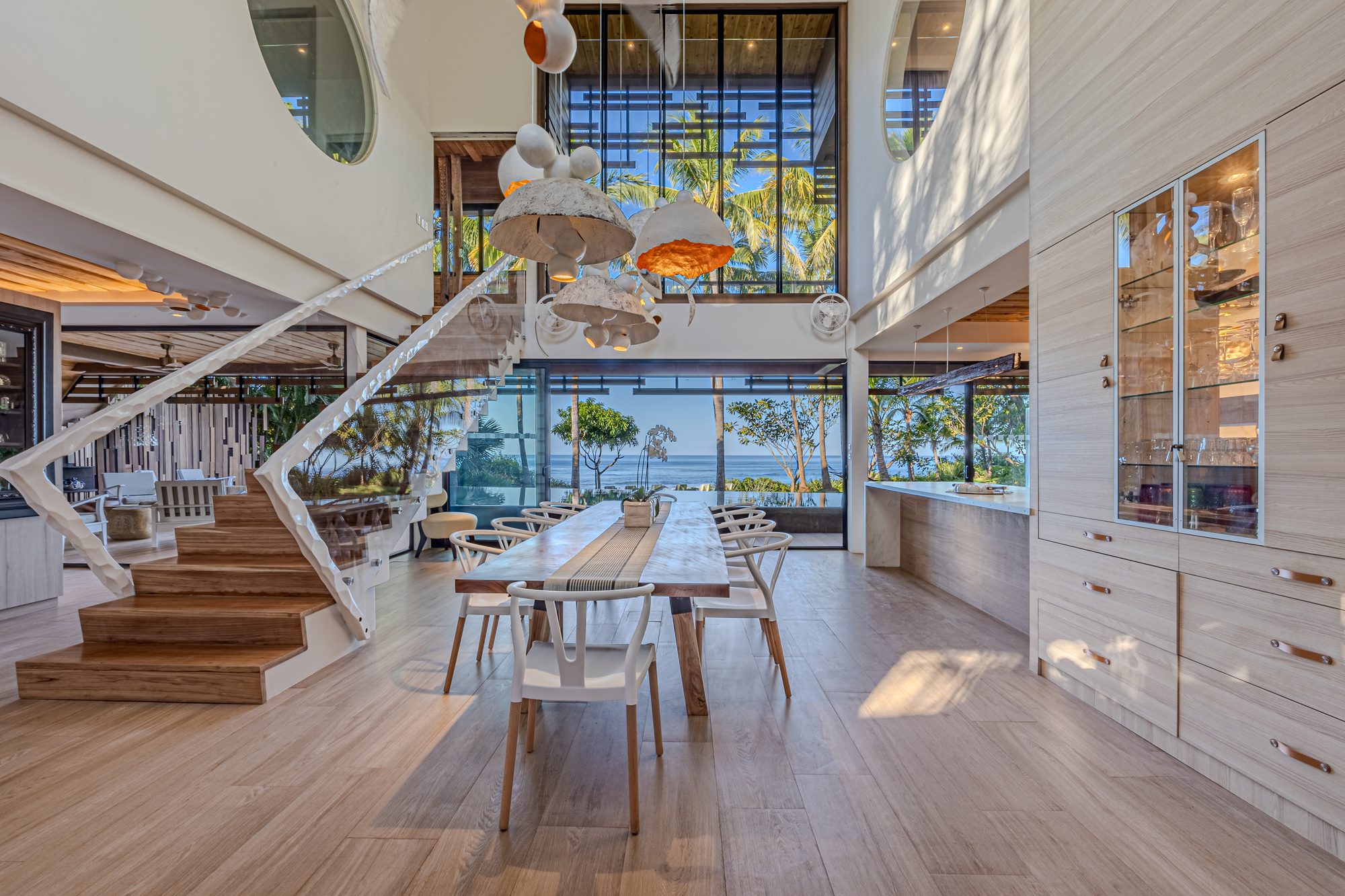 Dining area with sculptural staircase, artistic pendant lights and ocean view beyond.