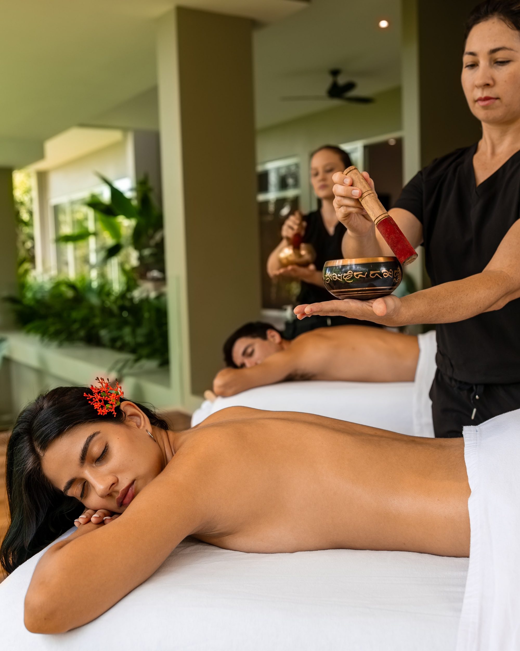 Therapists perform a Tibetan singing bowl massage on a couple at a spa.