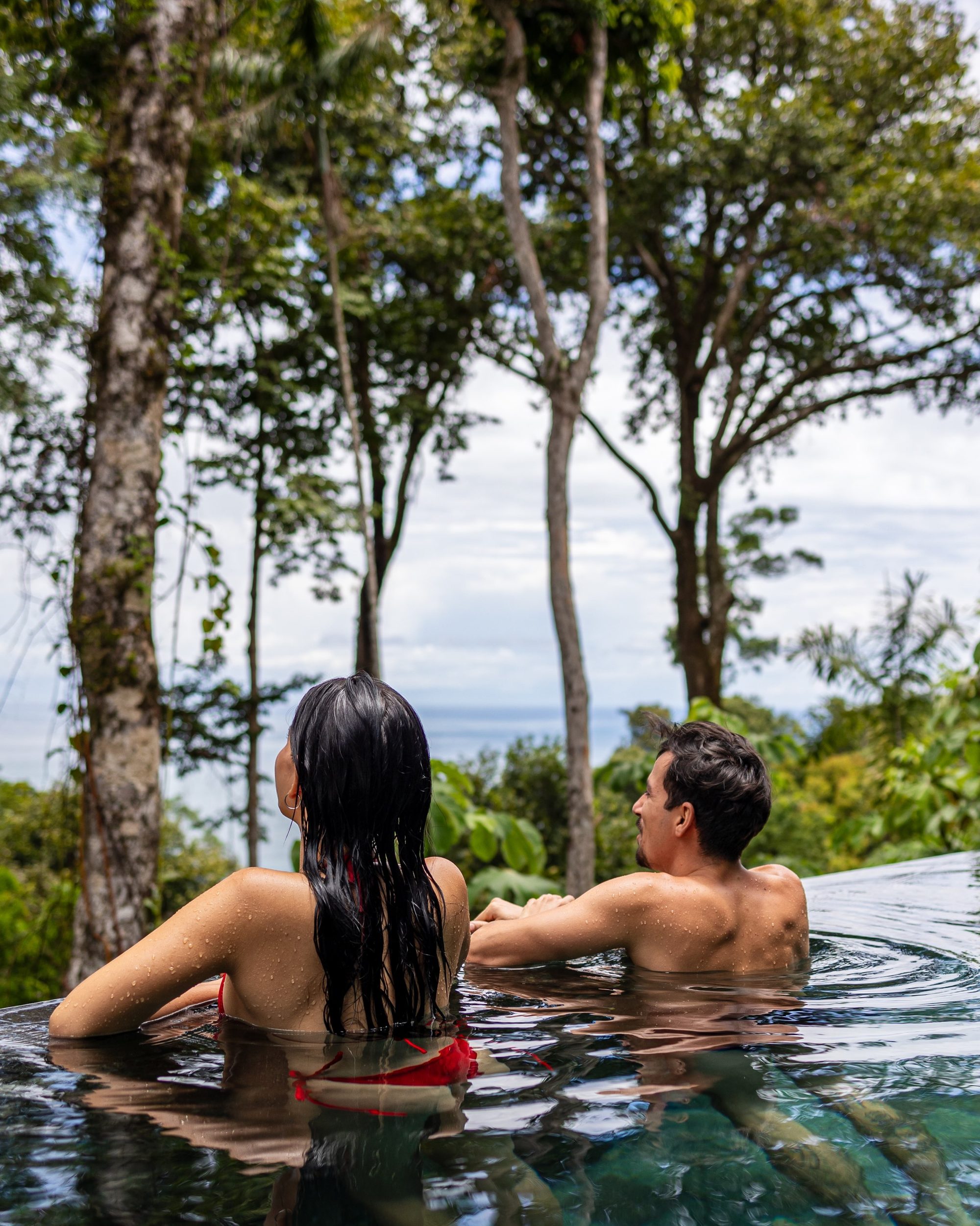 Couple relaxing in infinity pool surrounded by jungle with ocean view
