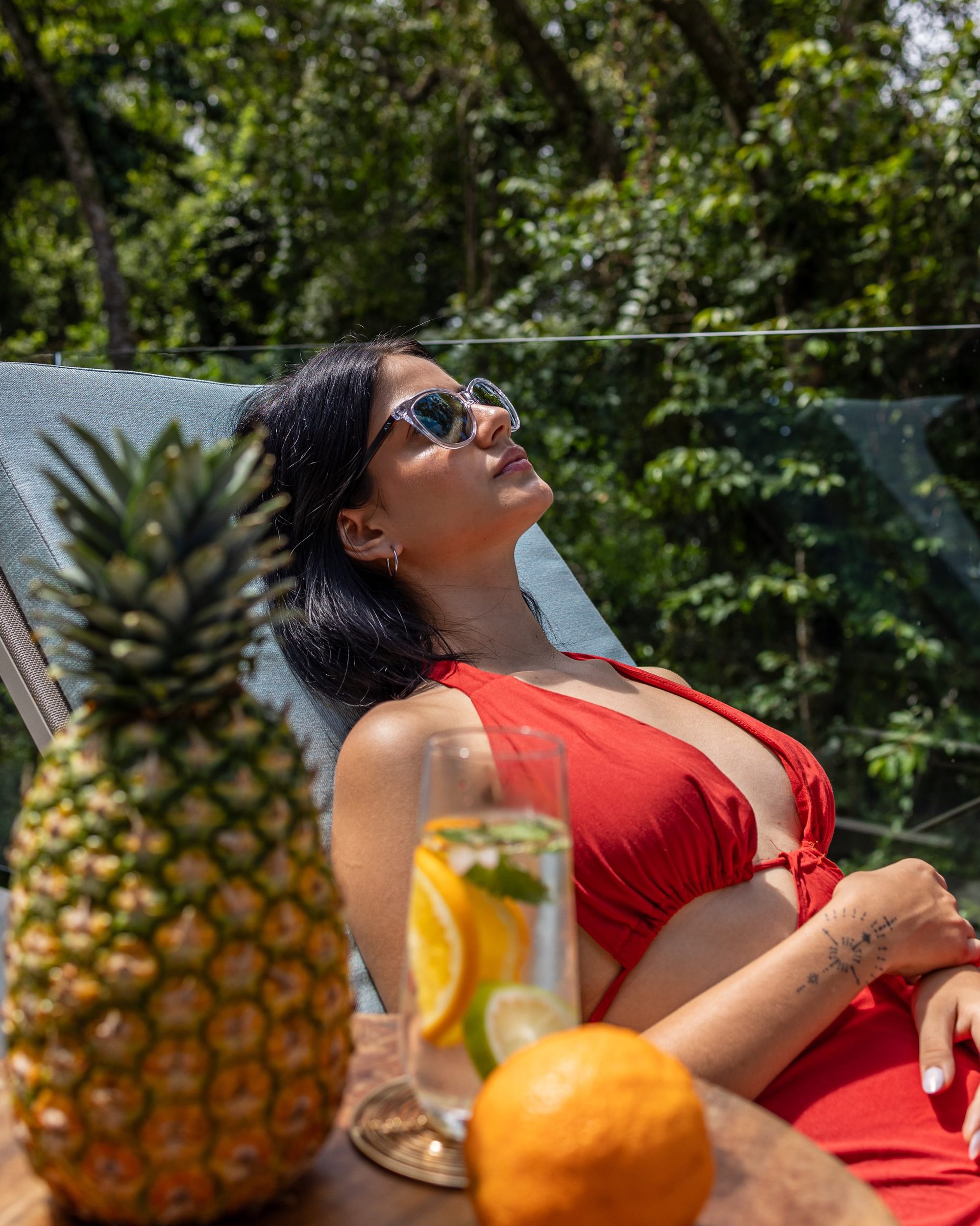 Mujer con traje de baño rojo se relaja al sol junto a frutas frescas y un cóctel