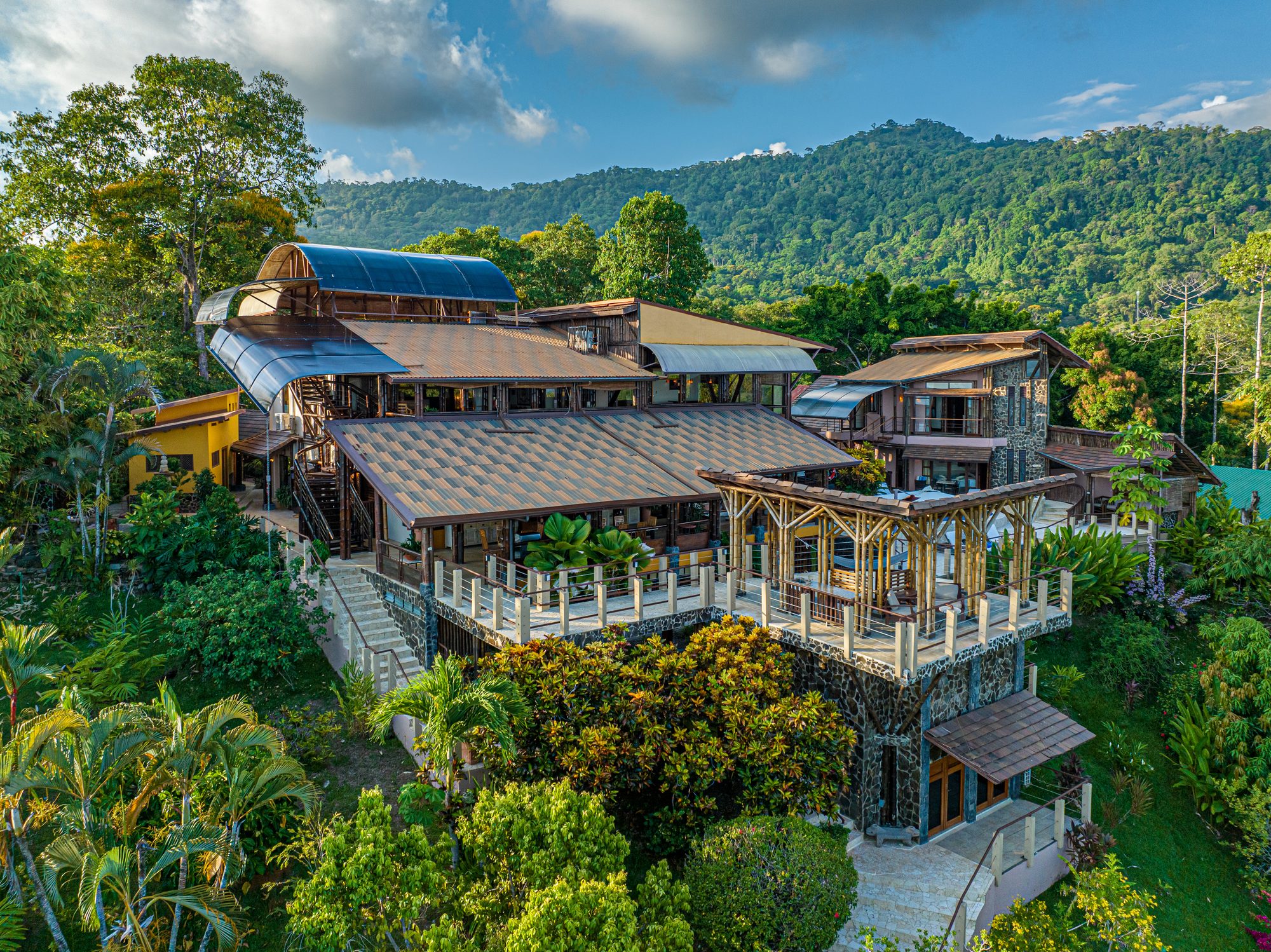 Vista aérea de una villa de lujo con techos de metal rodeada de selva tropical.