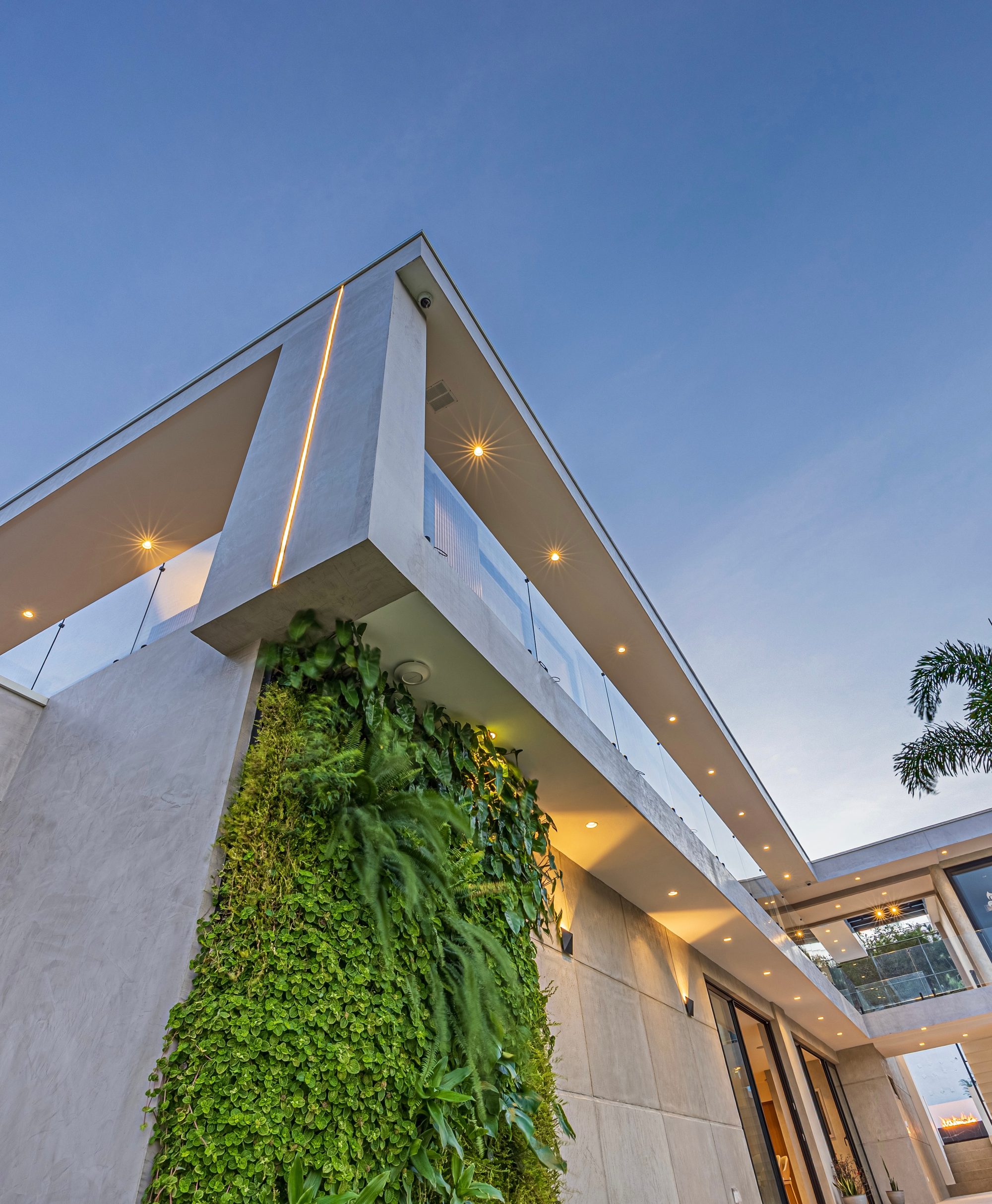 Upward view of a modern facade with a vertical living wall and warm lights at dusk.