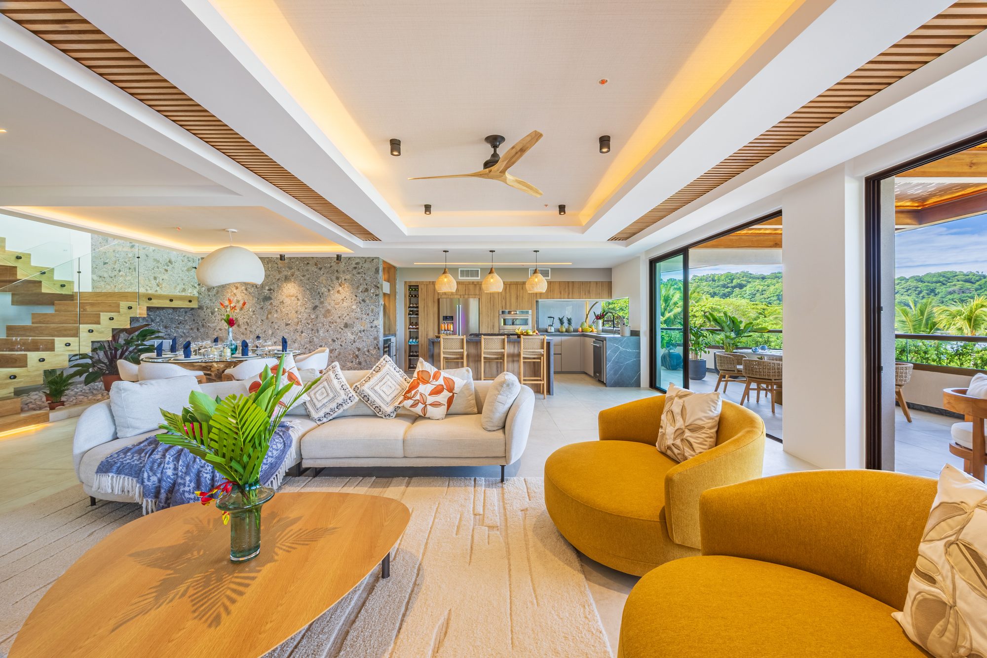 Spacious living room with jungle views and yellow armchairs beside the open kitchen.