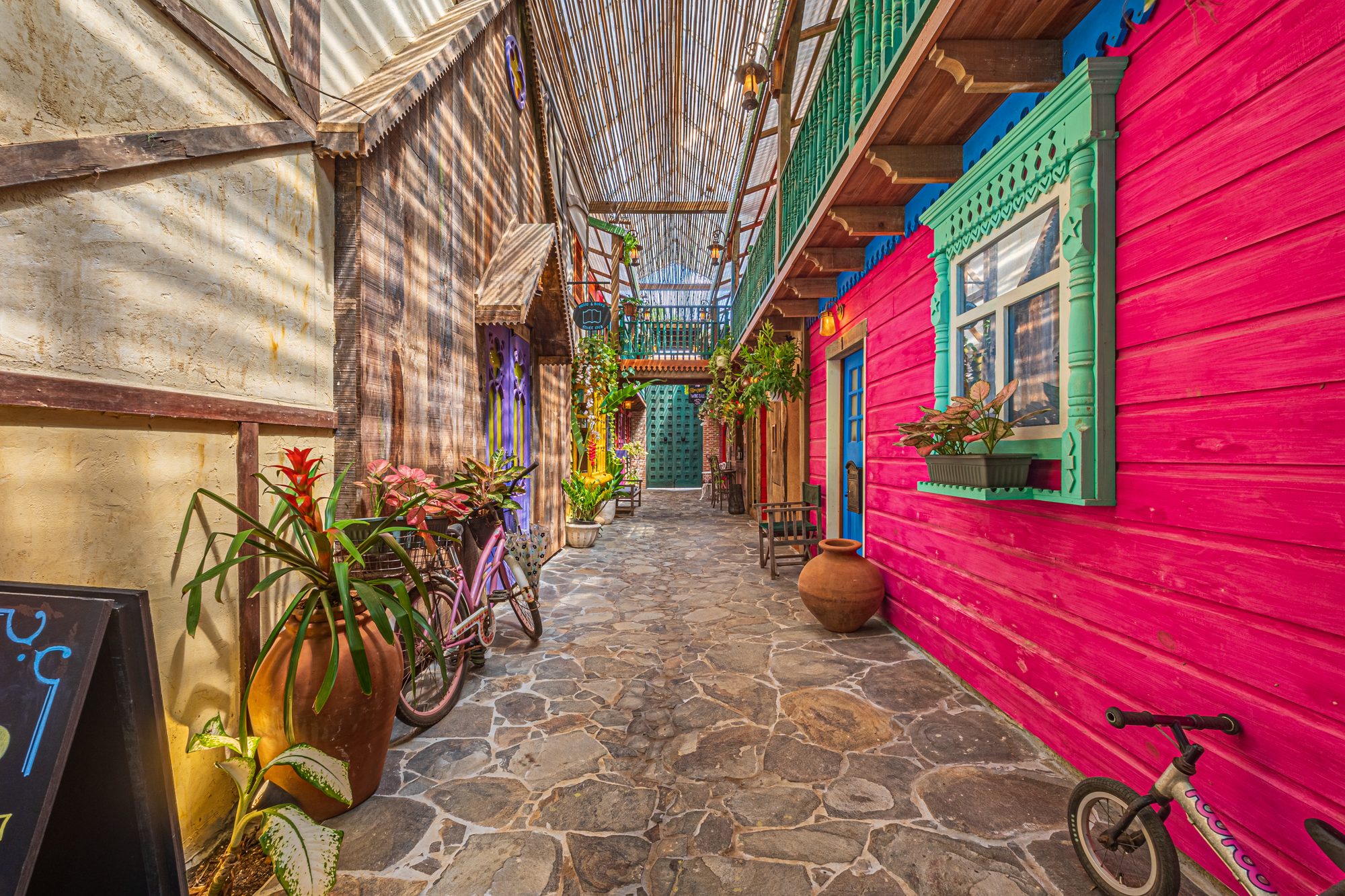 Stone-paved alley with vibrant colored facades, bicycles and potted plants.