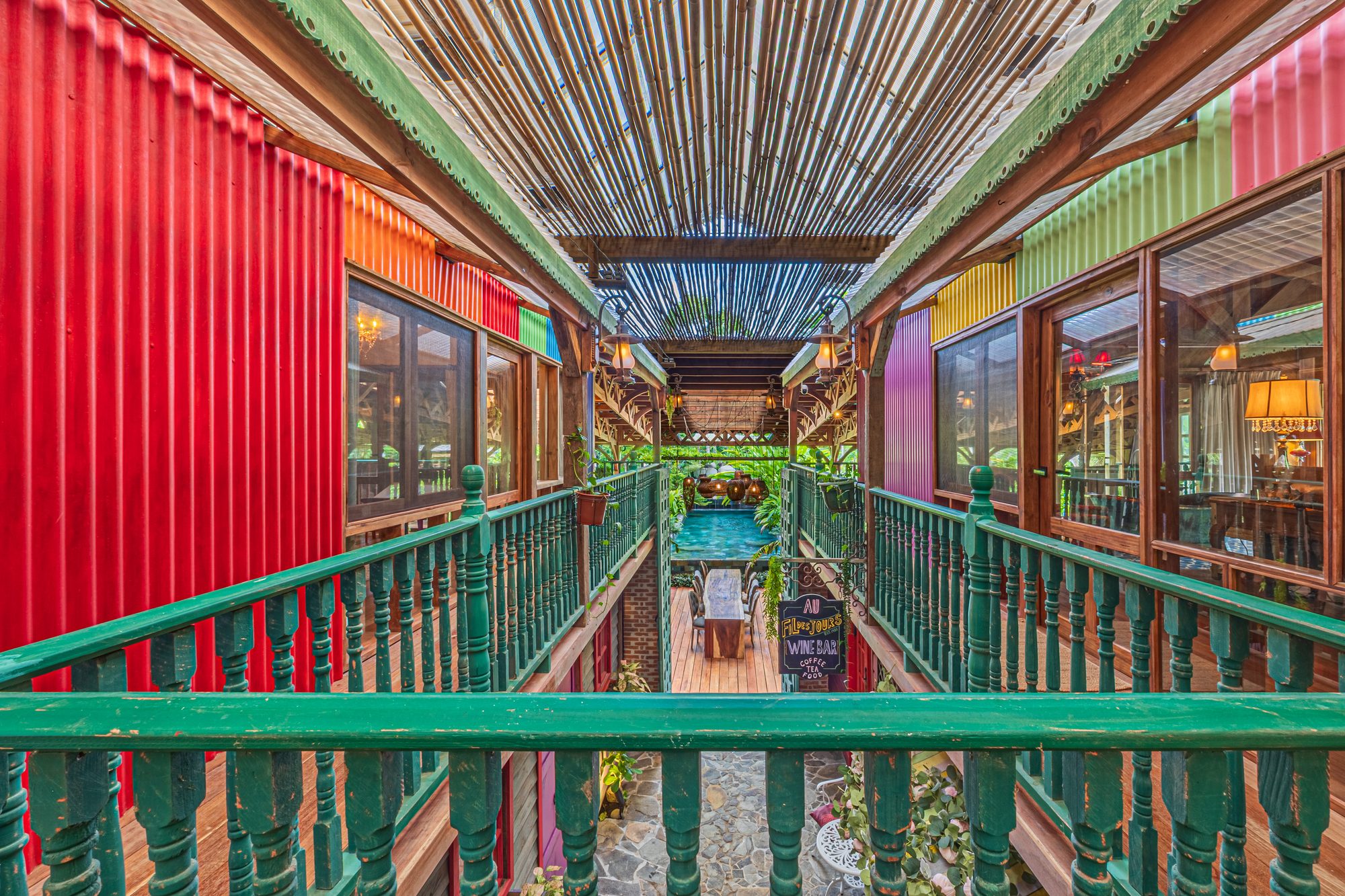 Elevated colorful corridor with bamboo roof leading to a pool area.