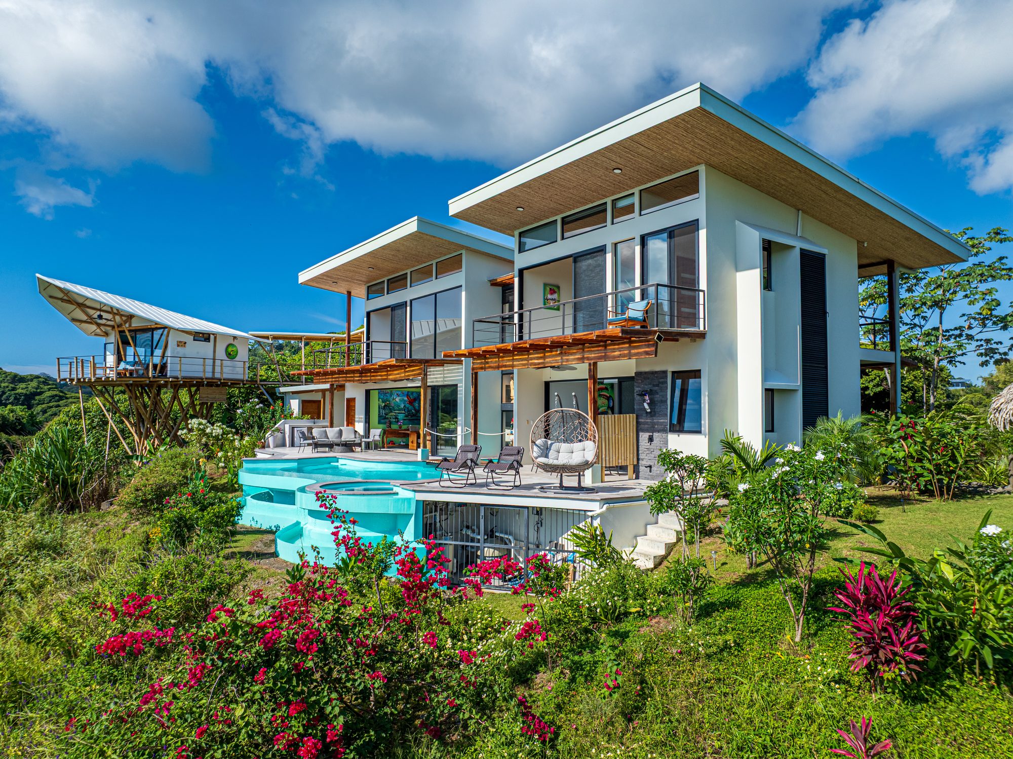 Casa moderna con piscina infinita rodeada de jardín tropical florido.
