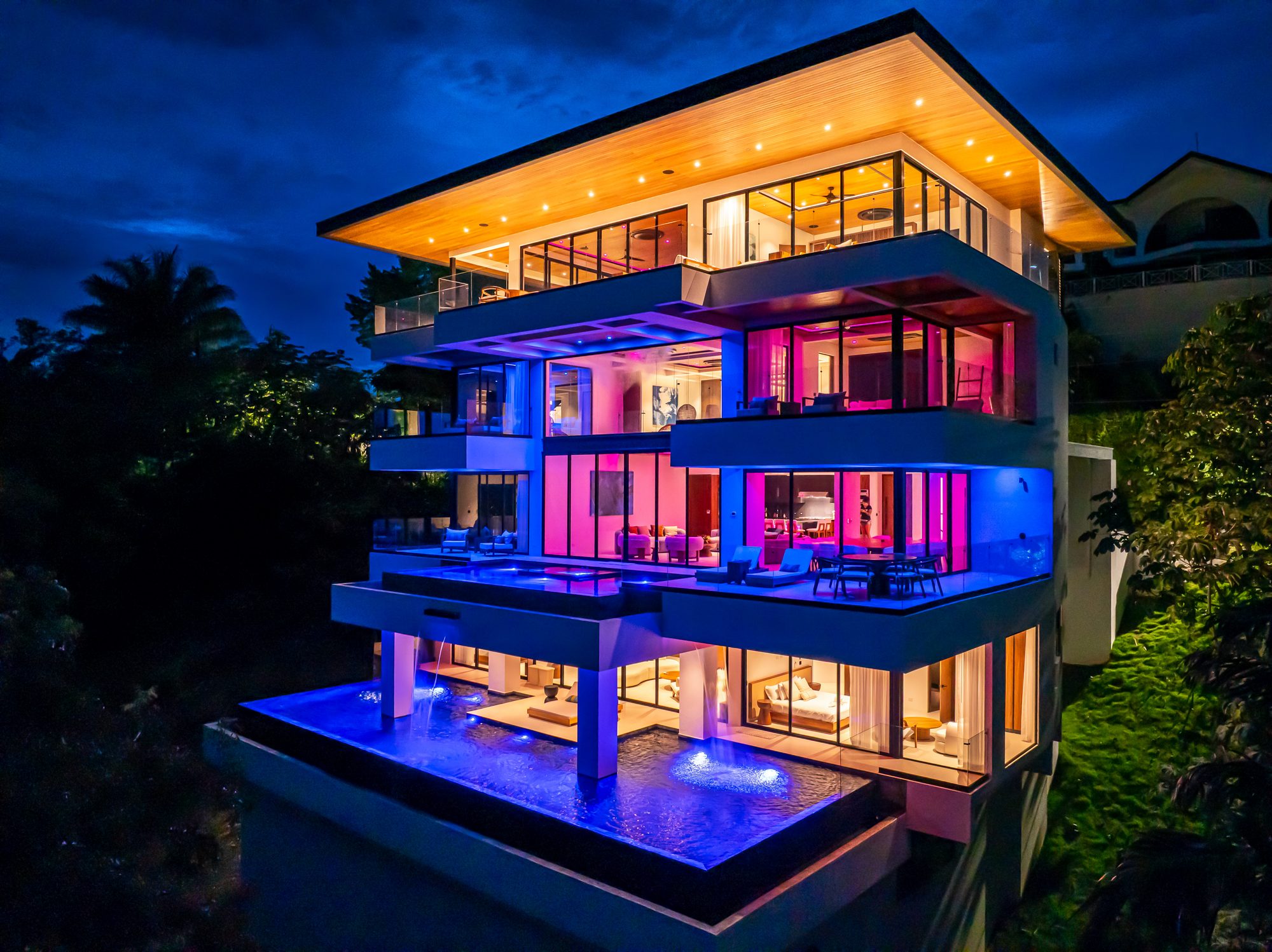 Luxury villa lit at night with tiered infinity pools and colorful led lighting.