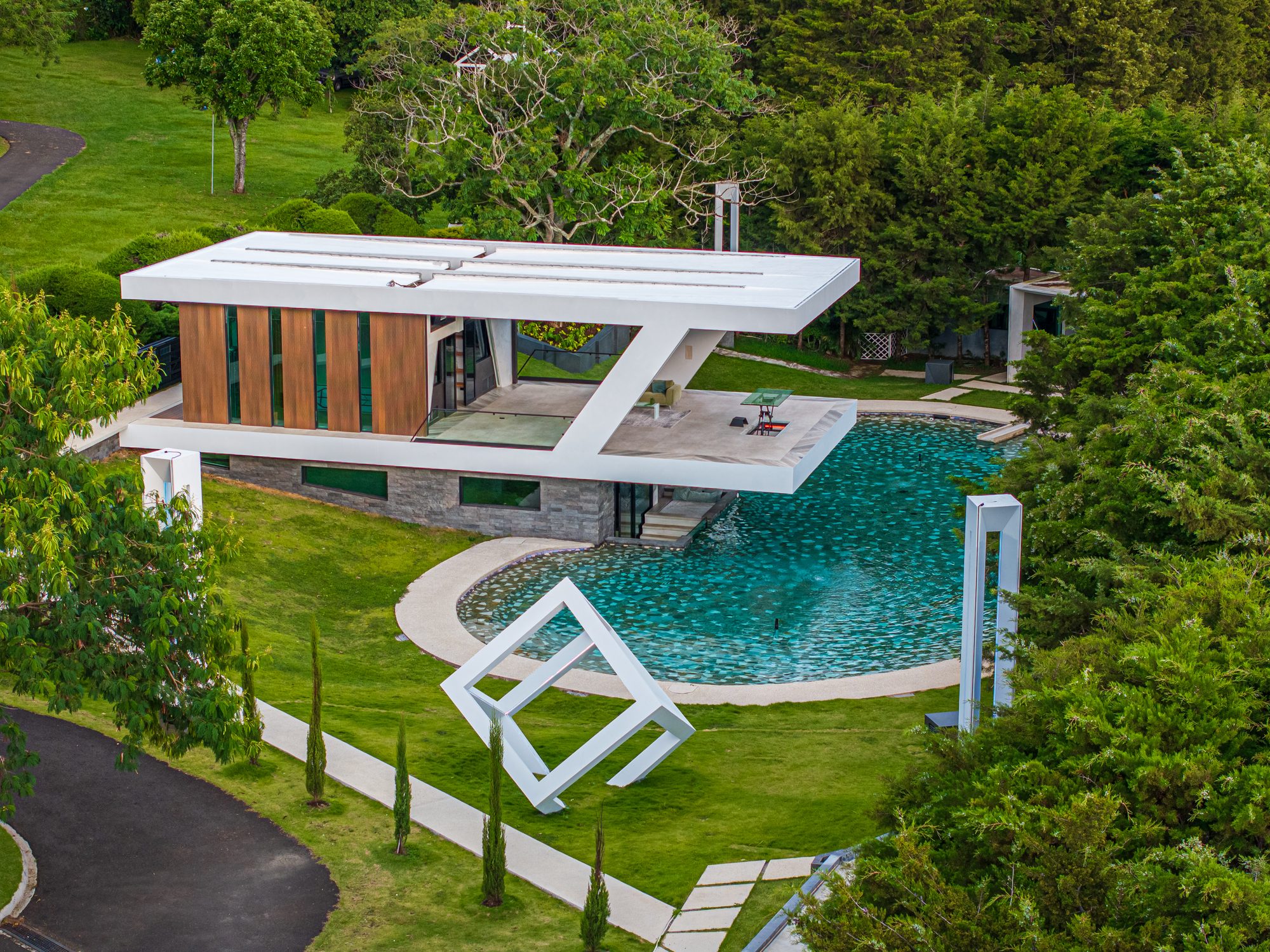 Aerial view of a modern house with a circular pool surrounded by lush greenery.
