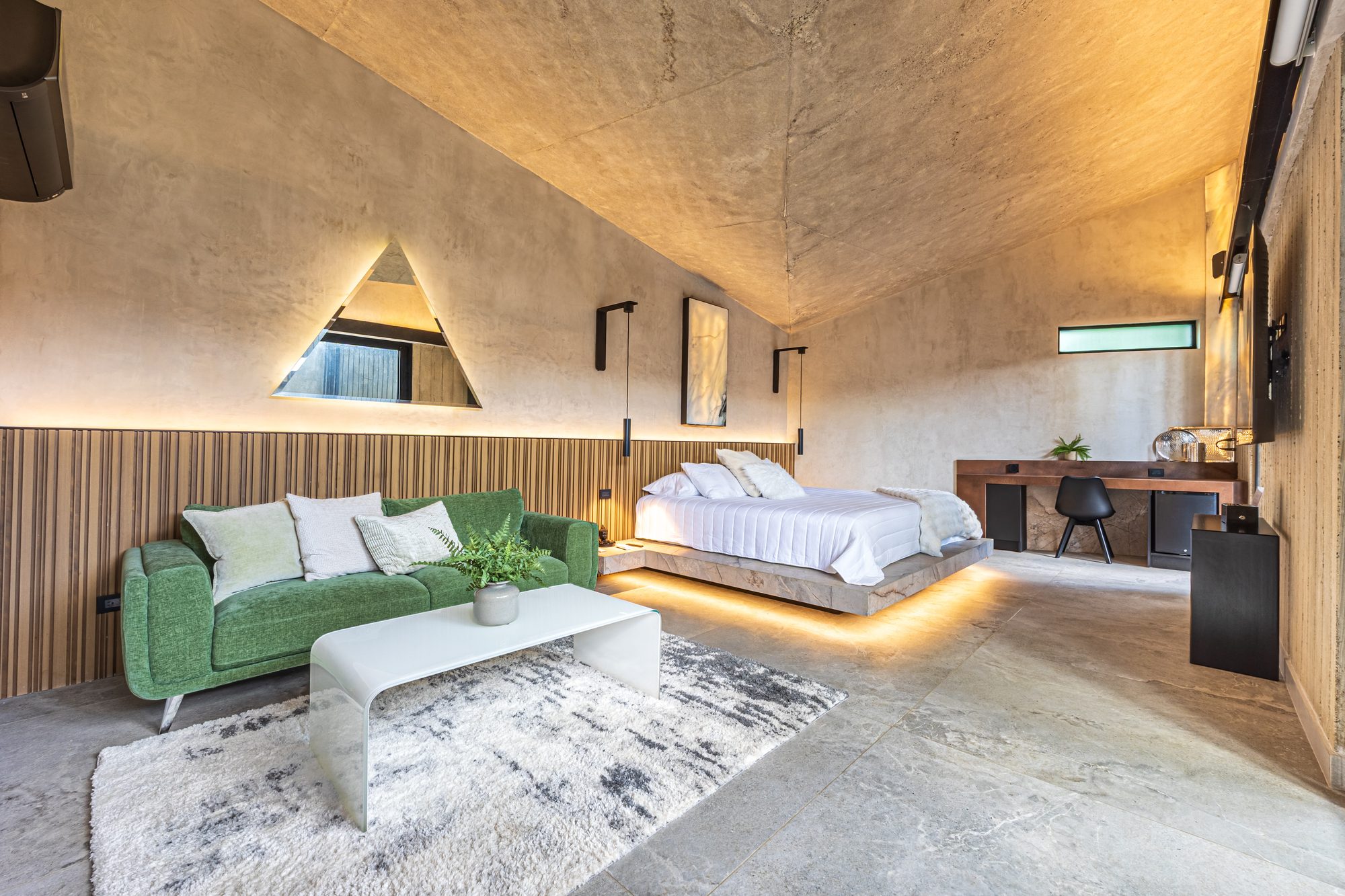 Suite with vaulted concrete ceiling, green sofa and illuminated floating bed.
