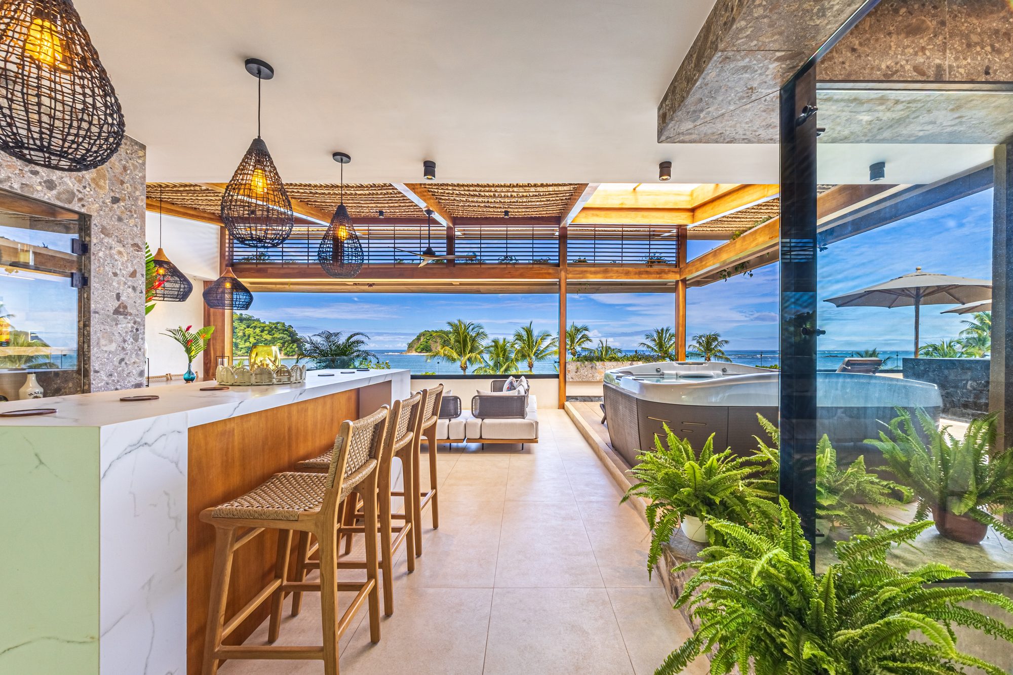 Terraza de lujo con jacuzzi, bar y vista al océano entre palmeras al atardecer.