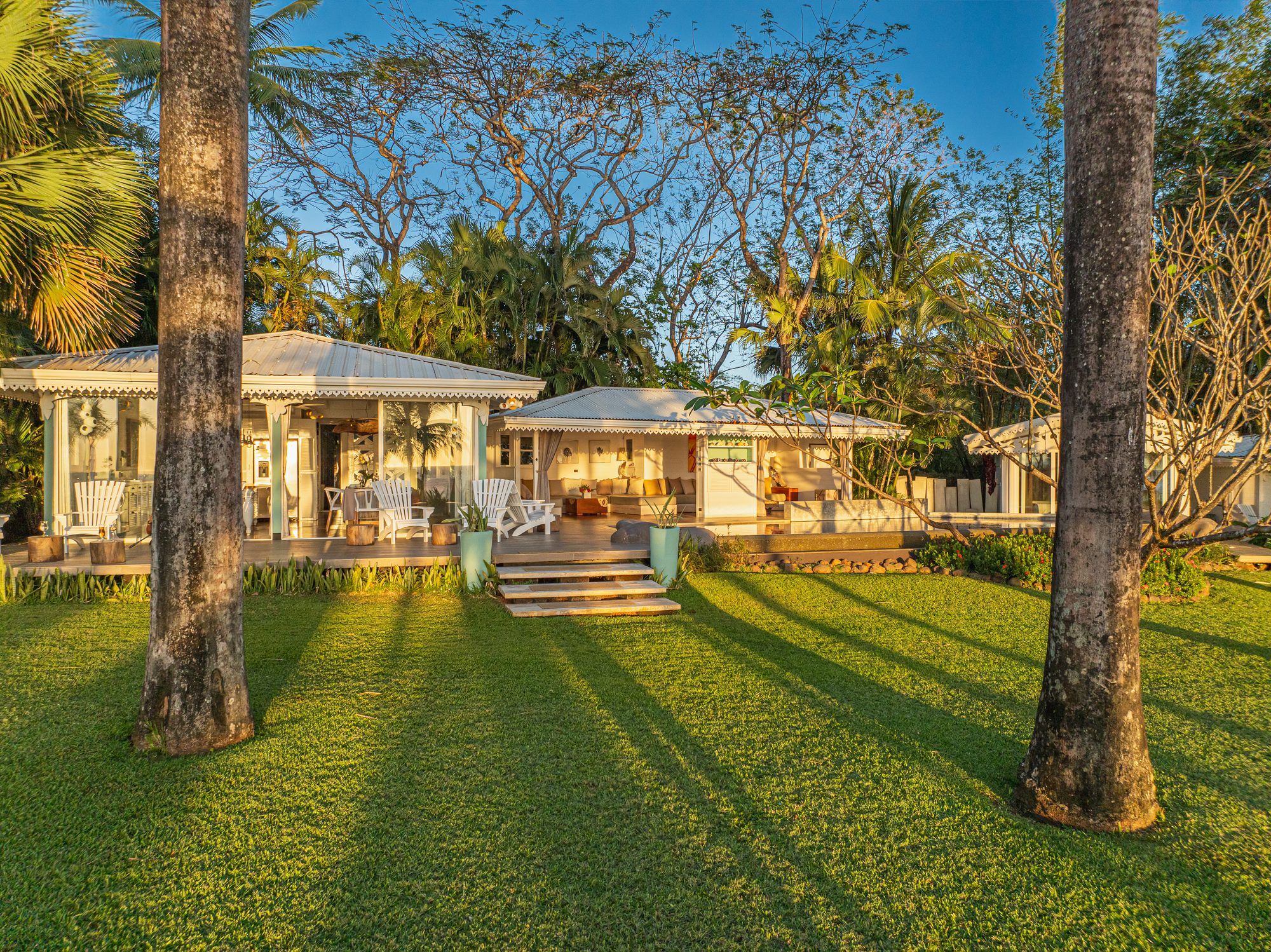 Tropical-style house with white roof surrounded by palm trees at sunset.