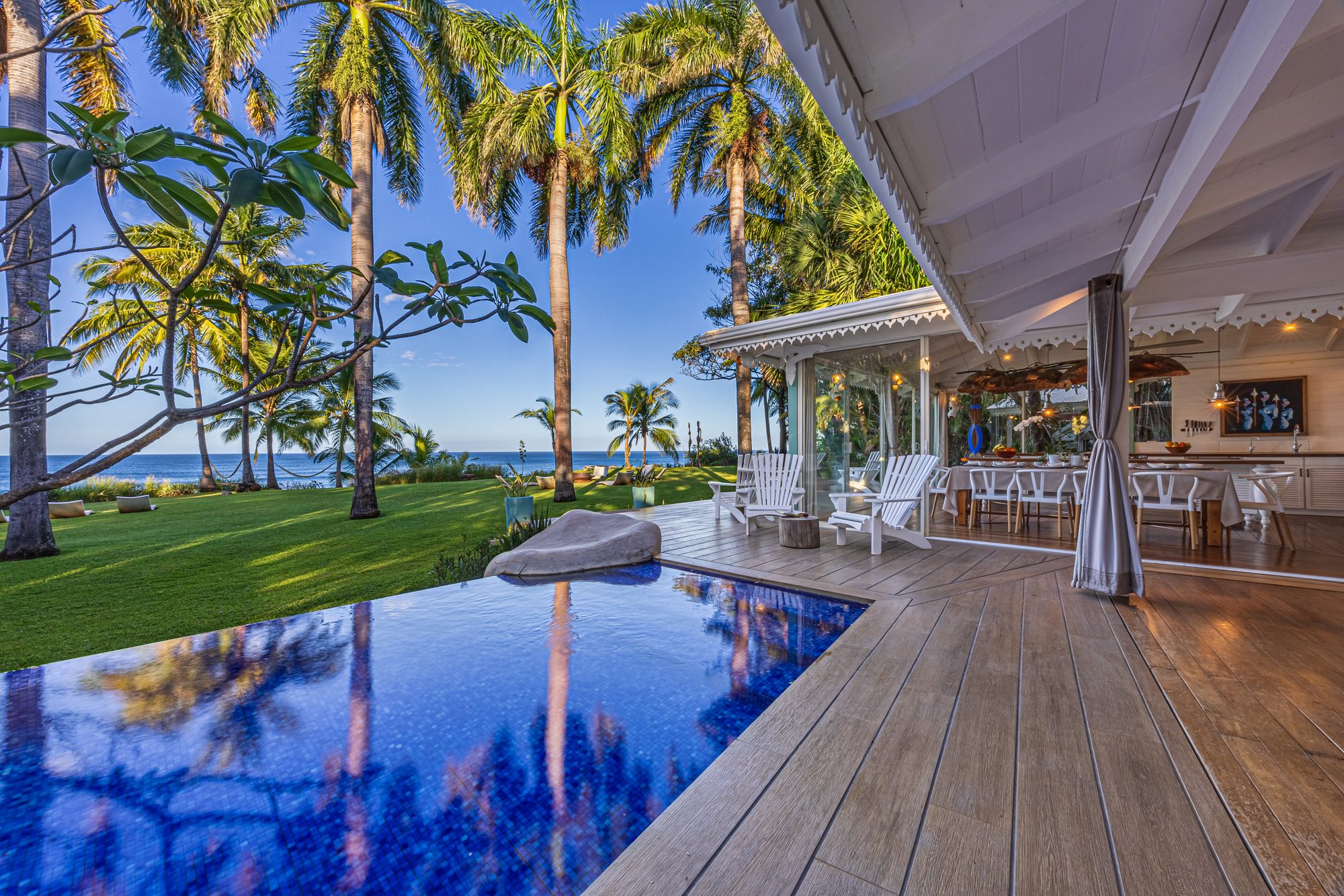 Infinity pool with ocean view surrounded by palm trees next to a wooden deck