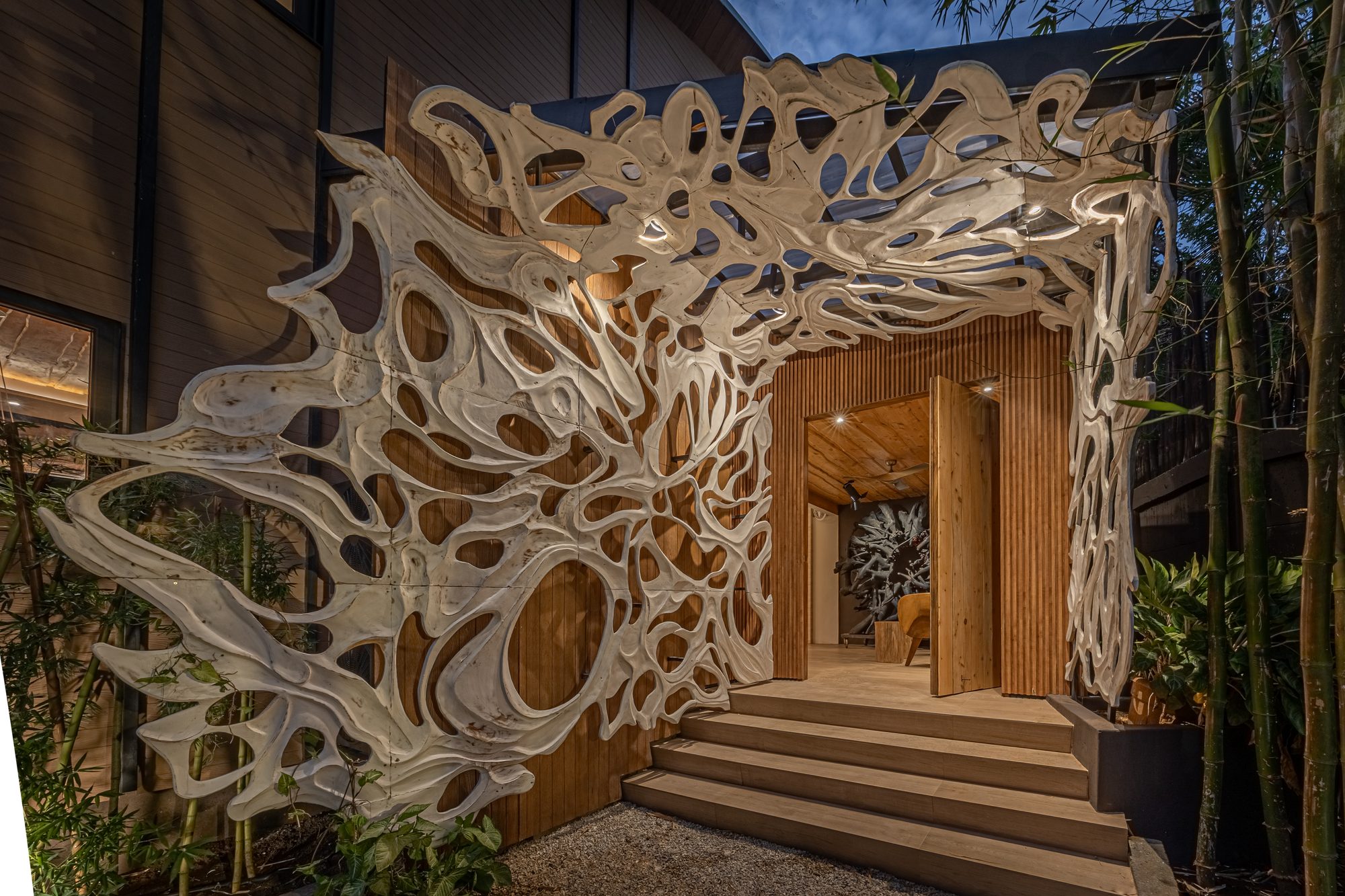 Entrada de casa con escultura orgánica de madera tallada sobre la puerta principal.