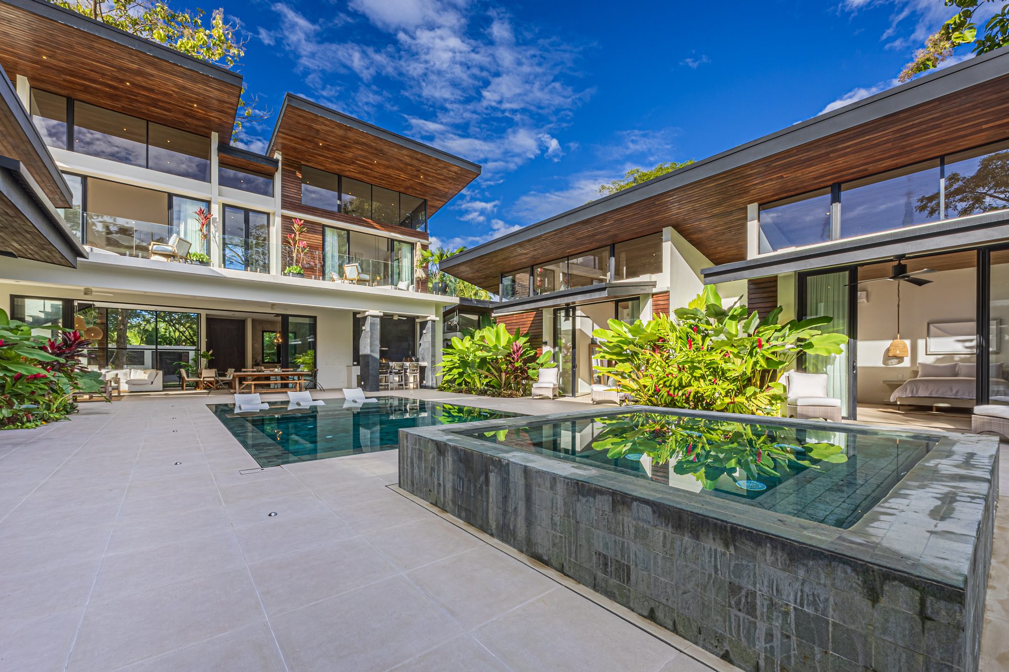 Modern villa with pool, jacuzzi and tropical gardens under a clear sky.