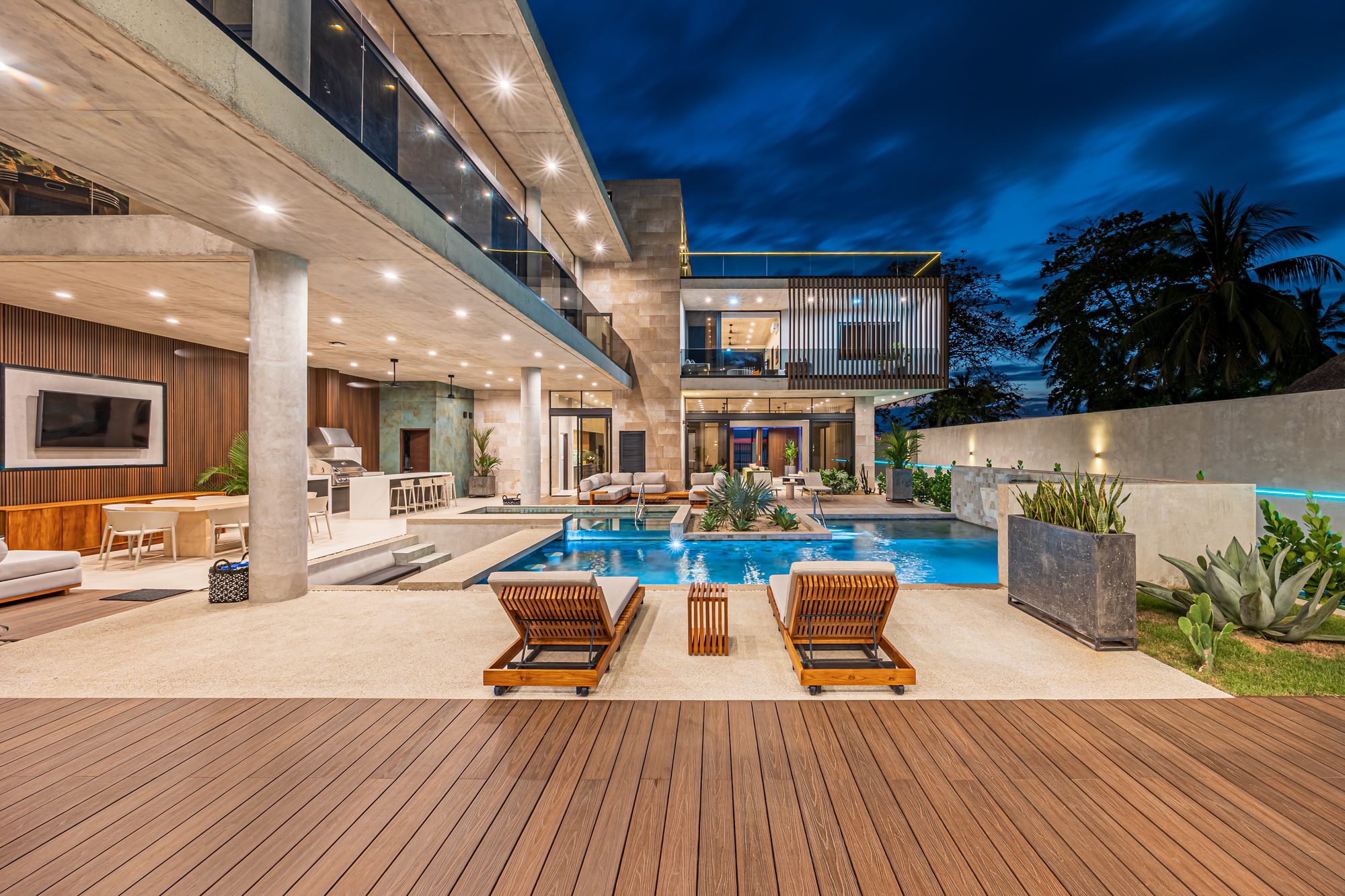 Piscina y terraza de lujo con camastros al atardecer frente a una villa moderna.