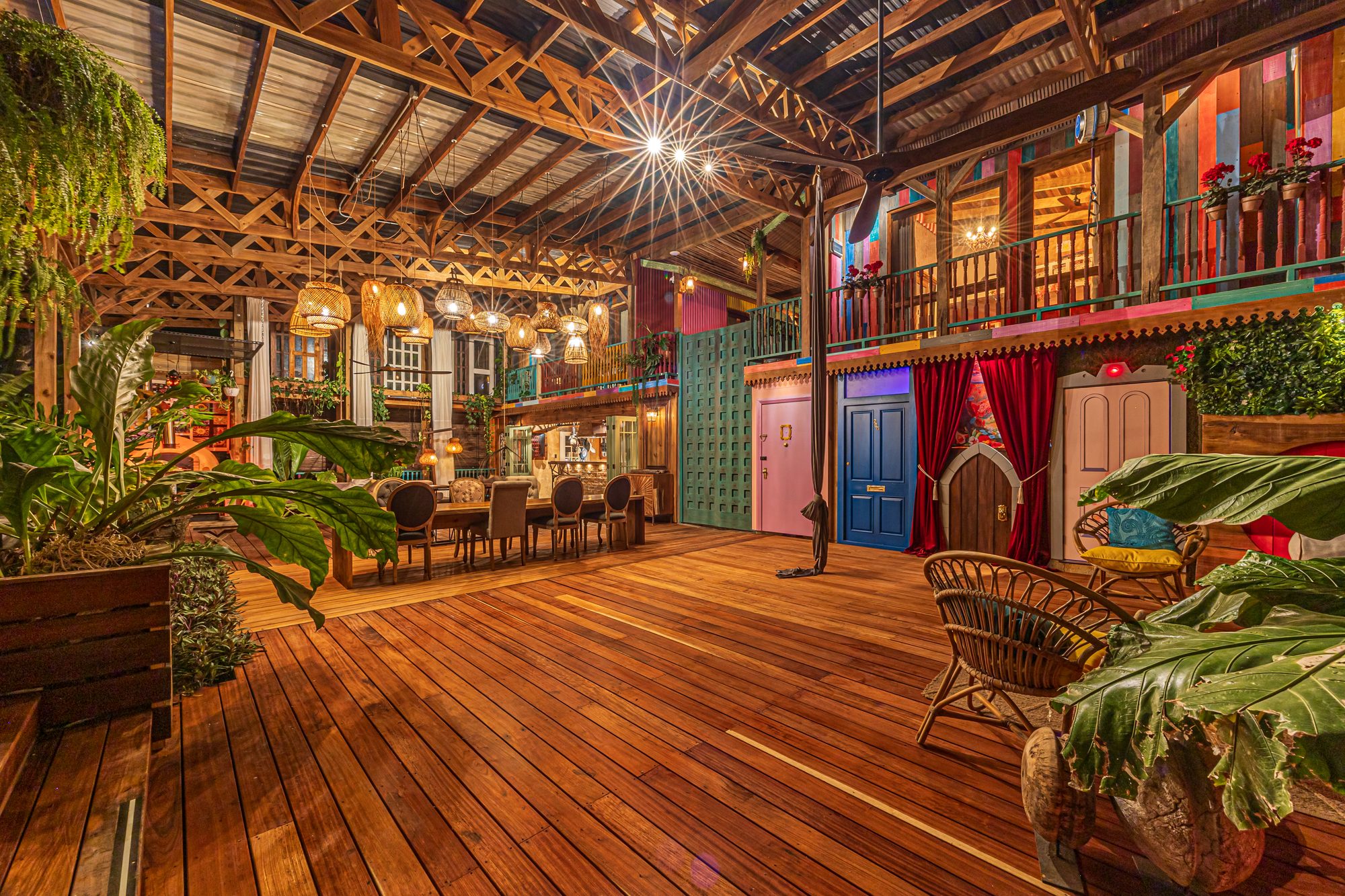 Salón techado con piso de madera, plantas tropicales y puertas de colores estilo boho.