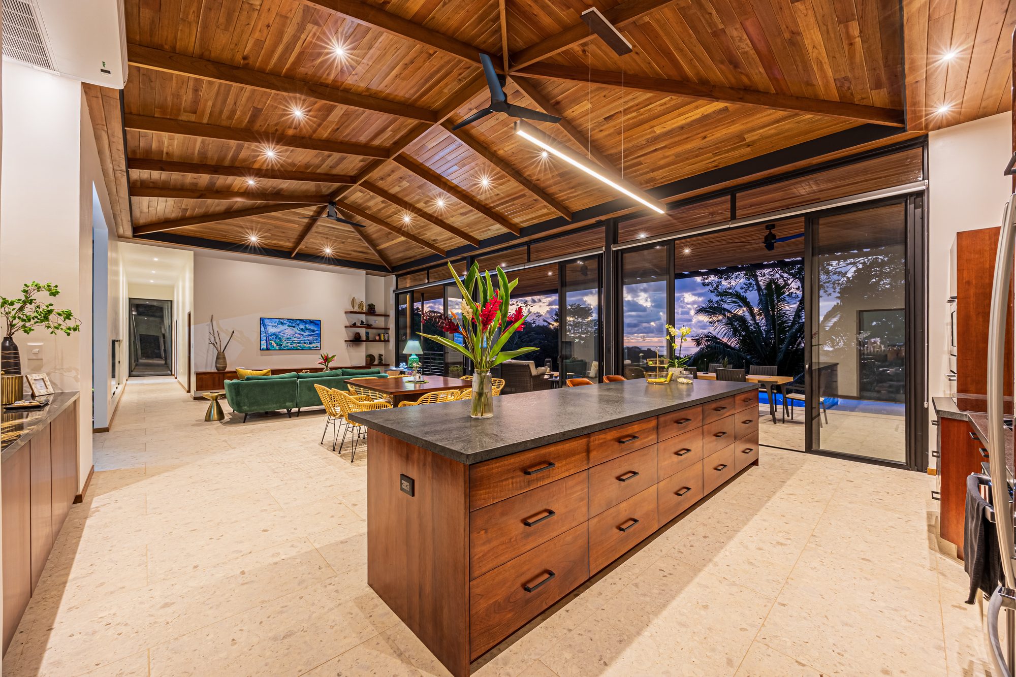 Open kitchen and living area with vaulted wood ceiling and tropical sunset view.