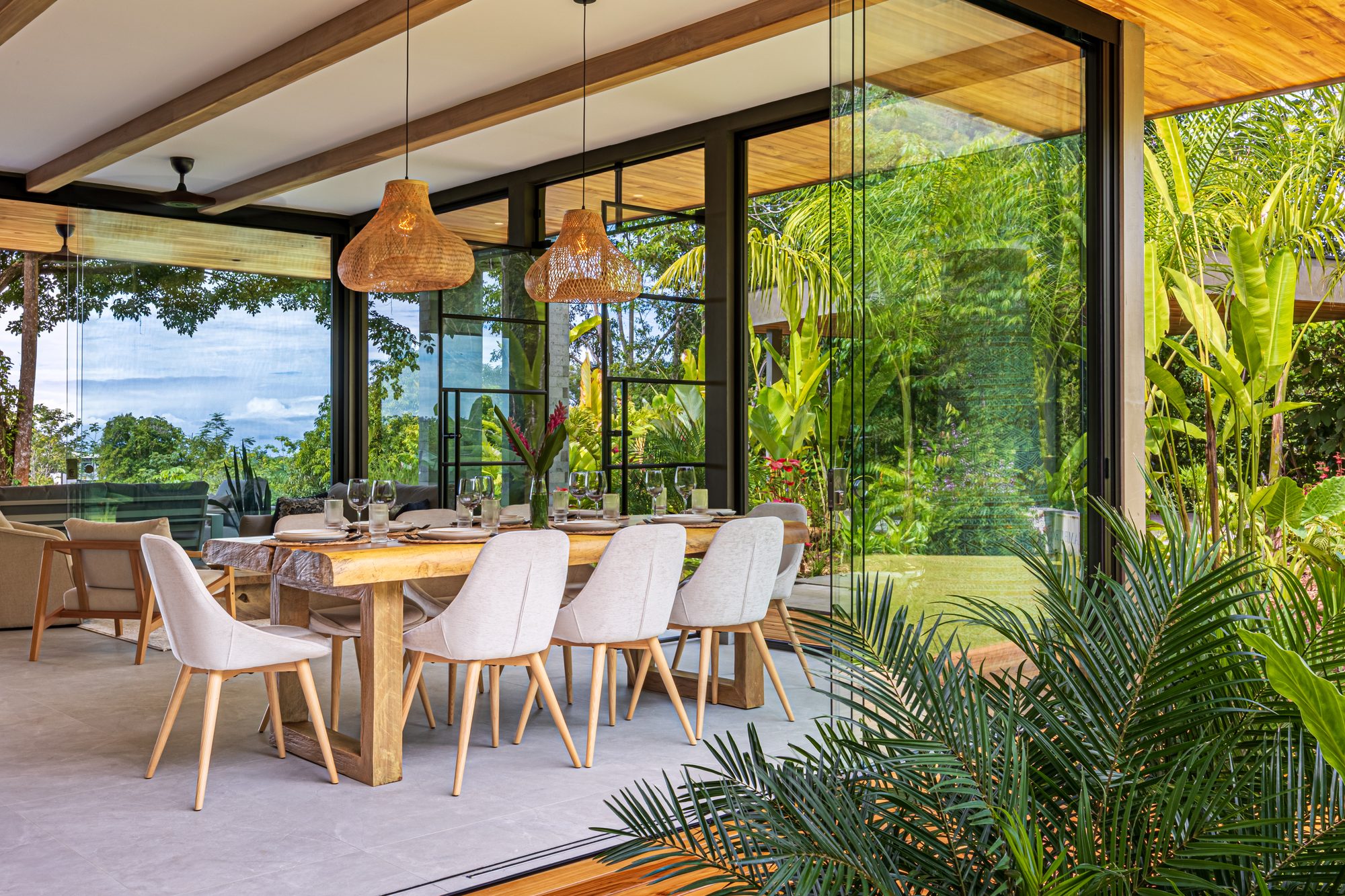 Comedor abierto con vista a la selva tropical y grandes ventanales corredizos.
