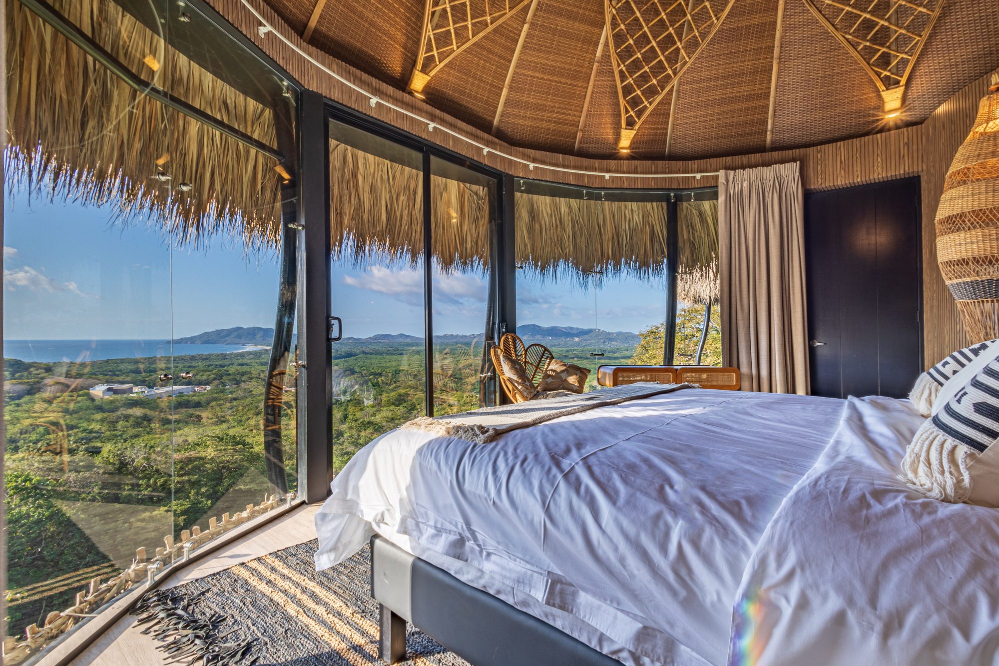 Bed with ocean view under a palapa roof in a luxury bedroom