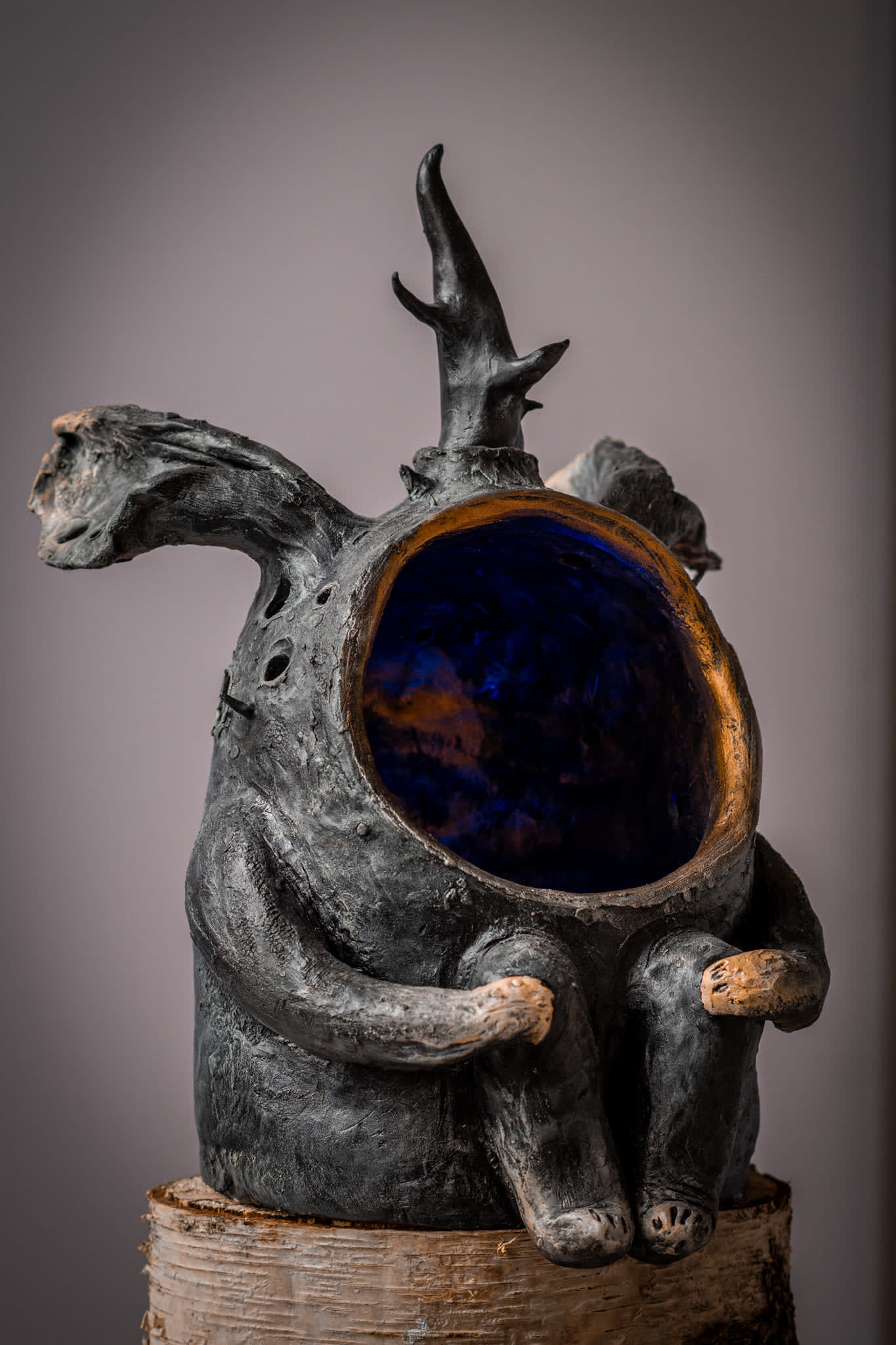 Horned ceramic creature holding a deep violet glass orb