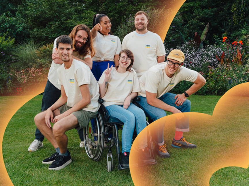 Een afbeelding van een groep mensen die samen lachen en een positieve sfeer uitstralen. Ze staan in een groene omgeving.