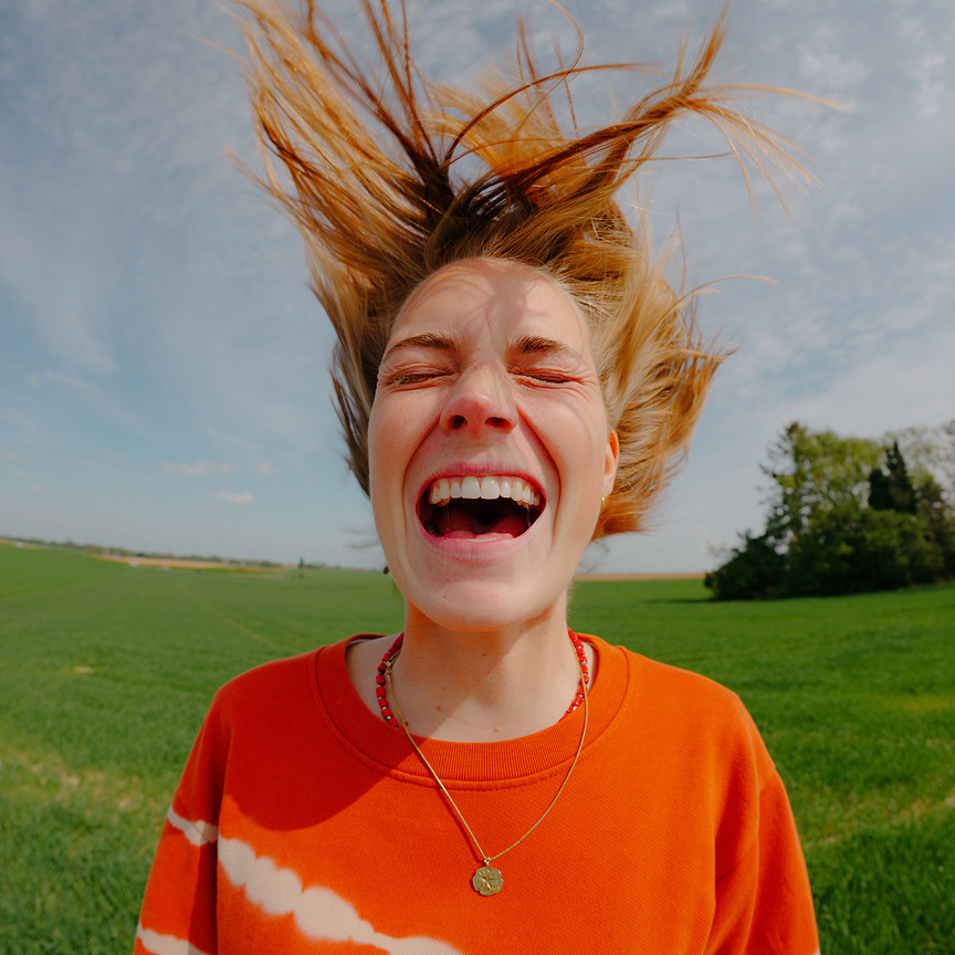 Vrouw met wapperend haar in de wind, lachend en stralend, straalt positieve energie uit.