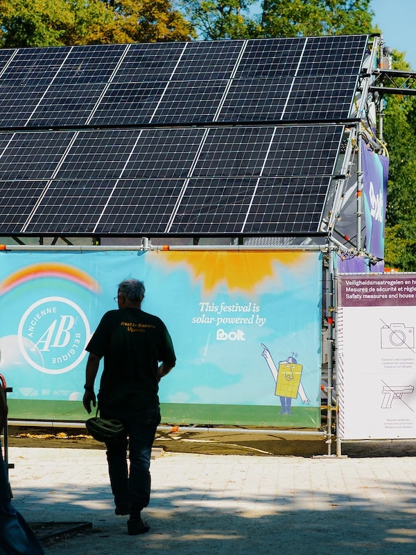 Een foto van een opwekker bij Bolt die er gelukkig uitziet. Hij staat met 1 voet op een zonnepaneel. In een zomerse setting