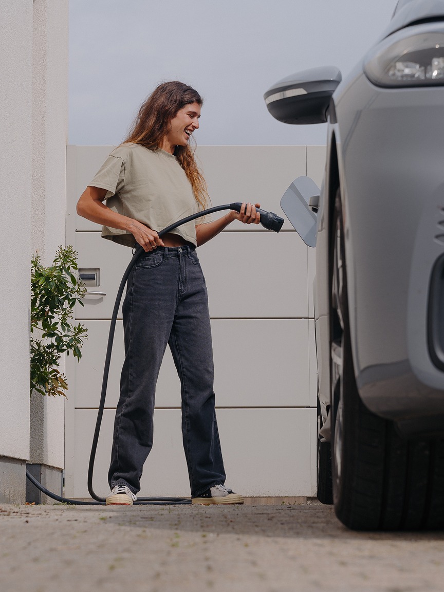 Lachende vrouw die haar elektrische auto laadt.