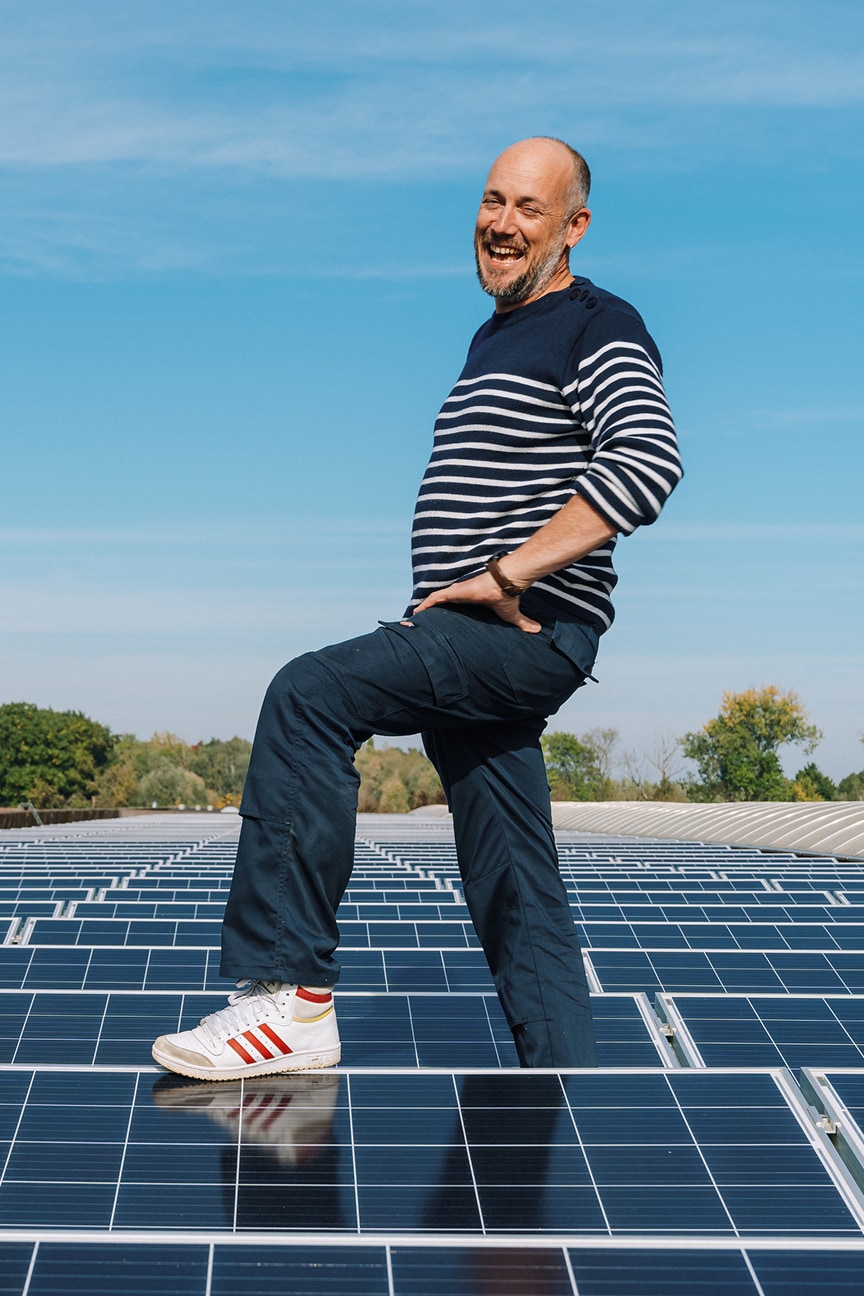 Een blije man (opwekker) die met trots bij zijn zonnepanelen staat in een zonnige omgeving.