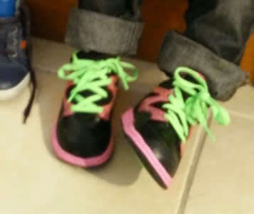Une paire de tennis majoritairement noires, à la semelle rose et aux lacets verts fluo