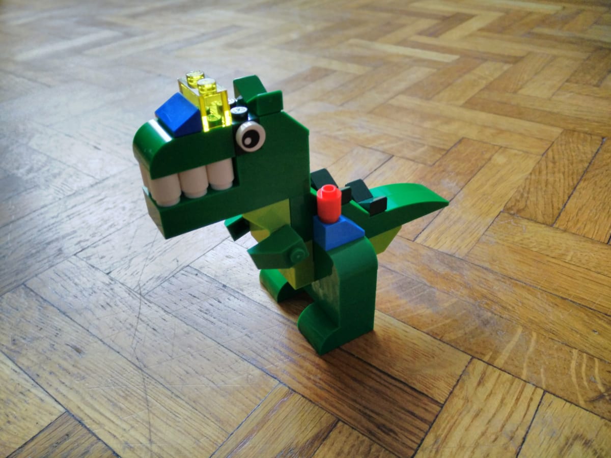 Une créature en Lego, proche du tyranosaure, mais avec un rictus très forcé et des éléments colorés sur la gueule et les cuisses, lui donnant l'aspect d'être hybride avec une machine.