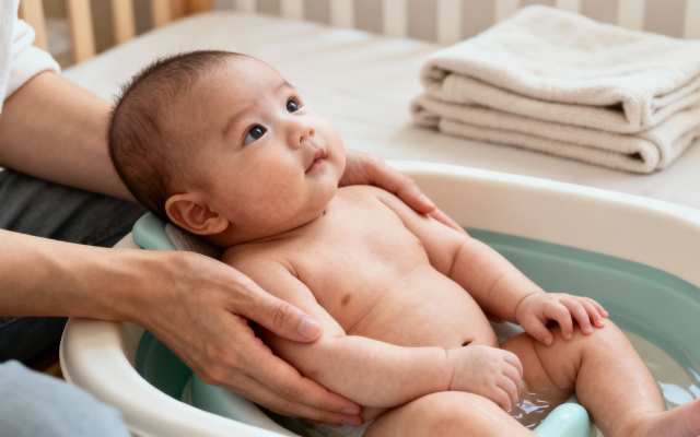 A content baby is taking a bath in a small tub, with an adult gently supporting.