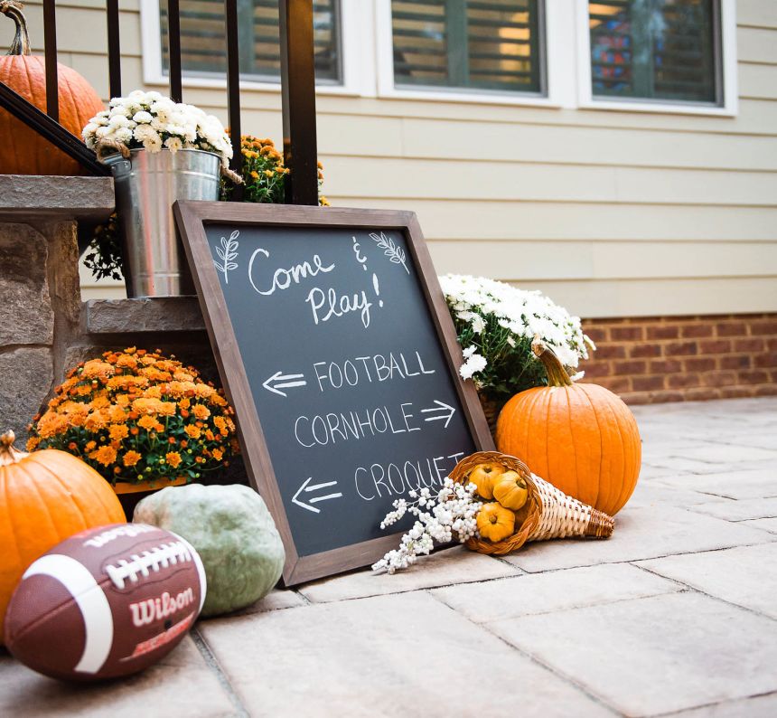 a wooden framed chalk painted glass is surrounded by pumpkins, mums and a football at the base of the backyard stone stairs