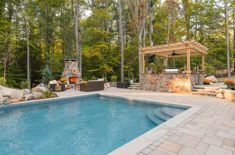 Outdoor space featuring a kitchen under a pergola, fireplace and fiberglass pool.